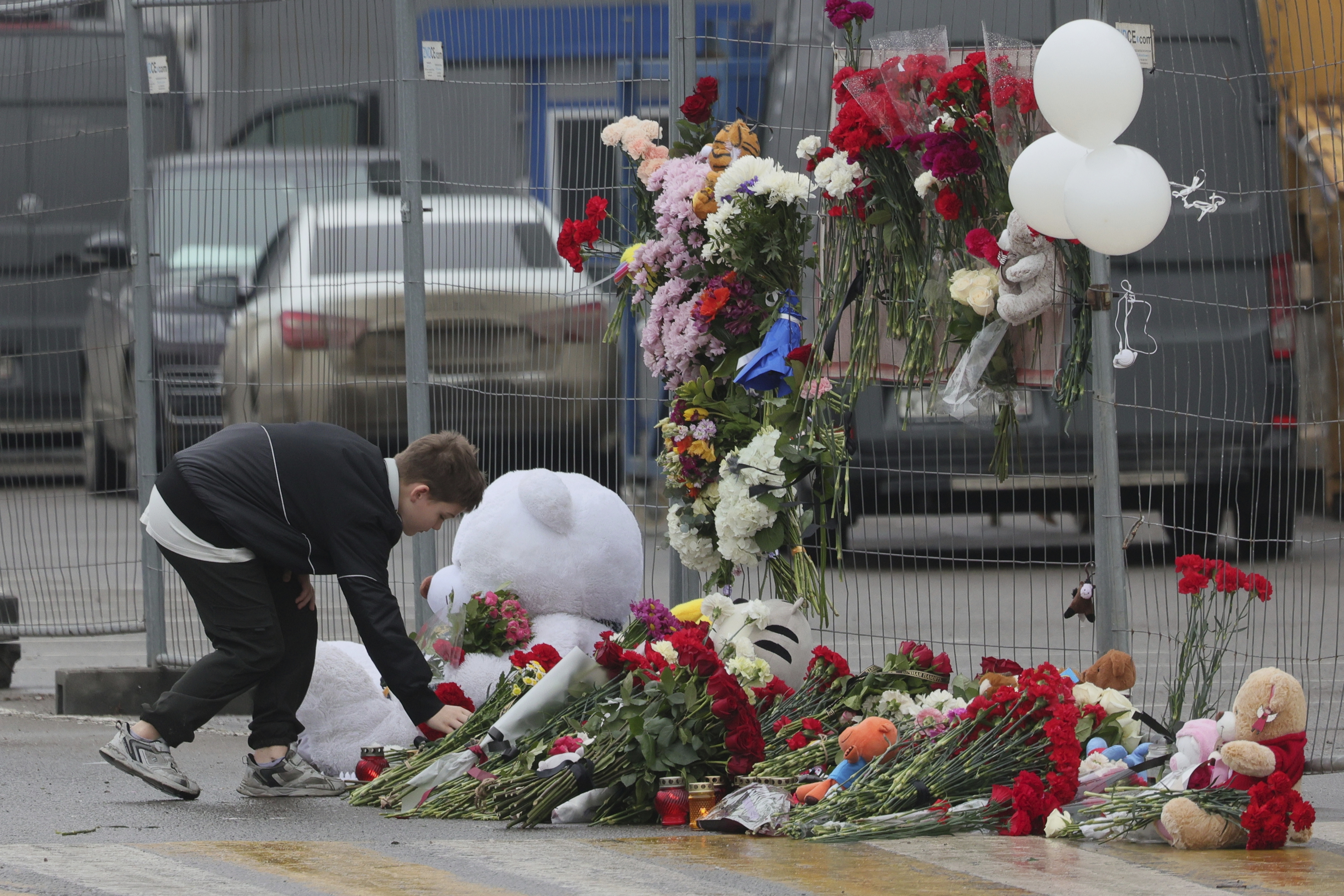 A boy places flowers at the fence next to the Crocus City Hall, on the western edge of Moscow, Russia, Saturday, March 23, 2024, following an attack Friday, for which the Islamic State group claimed responsibility. Russian officials say more than 90 people have been killed by assailants who burst into a concert hall and sprayed the crowd with gunfire. (AP Photo/Vitaly Smolnikov)