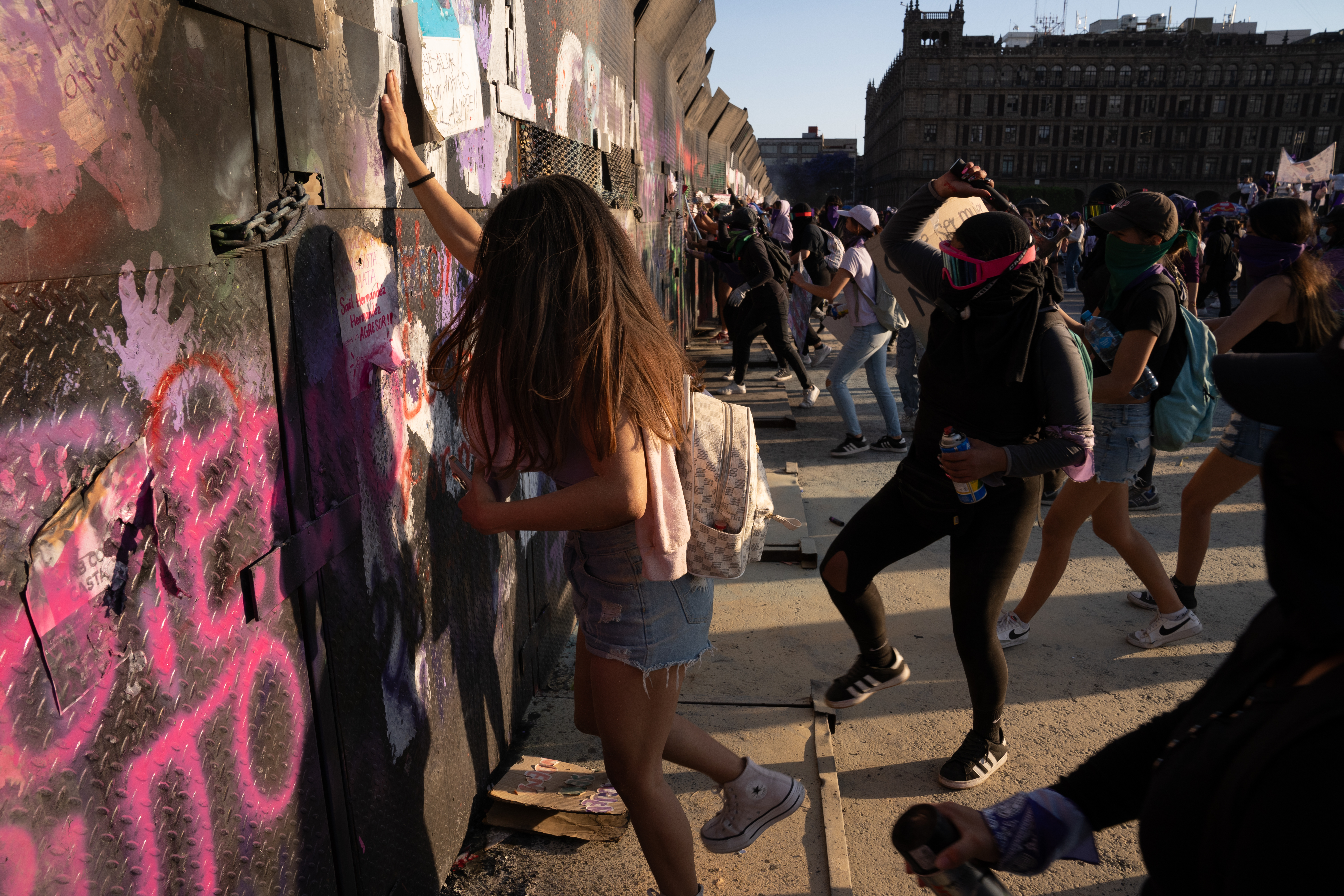 A woman calmly tries to attach a new poster to the metal barriers as the police fire chemical powder through the gaps, forcing them to run away. The police use fire extinguishers to fire the chemical powder that irritates eyes, skin and makes it difficult to breathe [Lexie Harrison-Cripps / Al Jazeera]