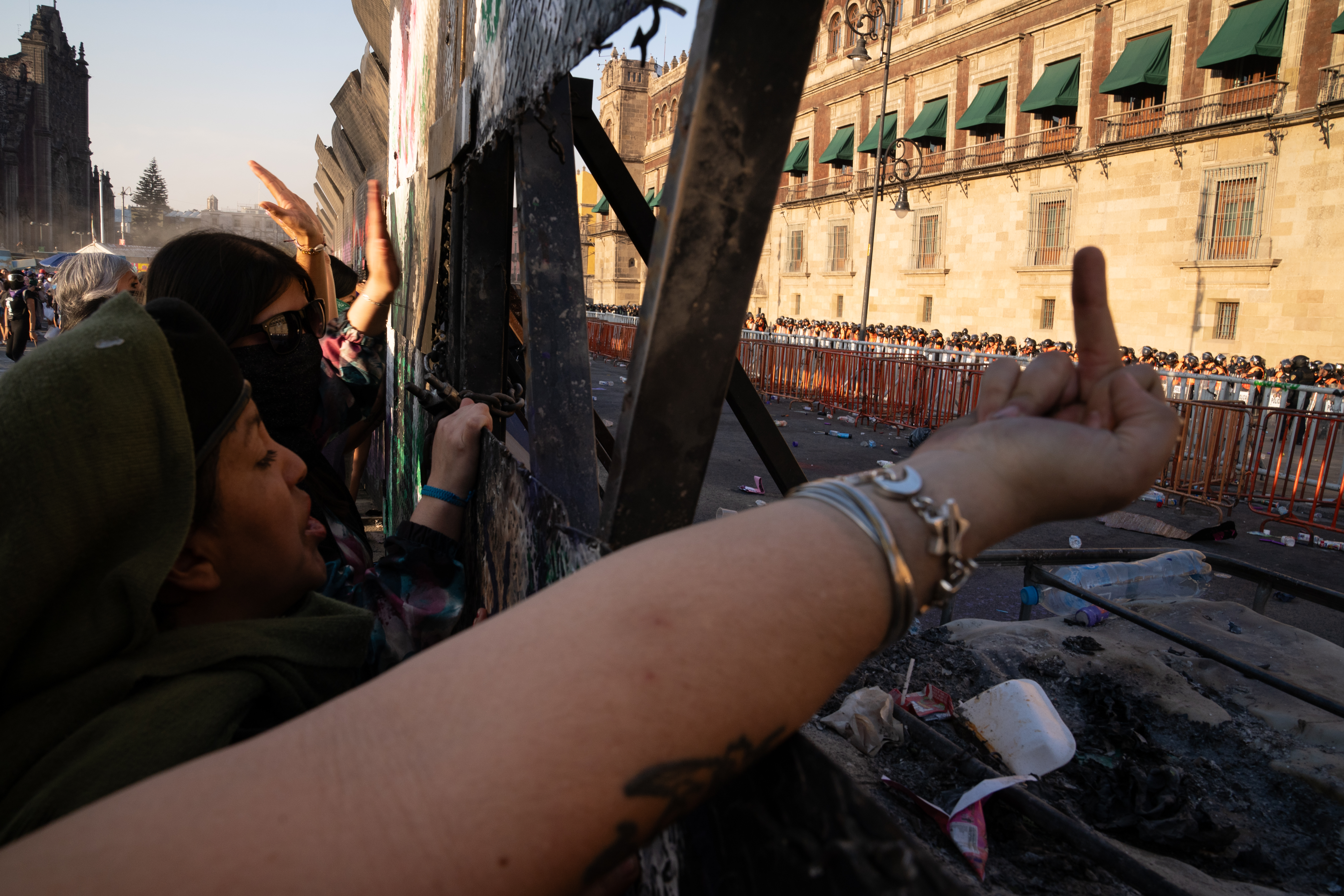A protester holds her finger up to the hundreds of police lined up safely away from the metal wall as other women bang and chant [Lexie Harrison-Cripps / Al Jazeera]