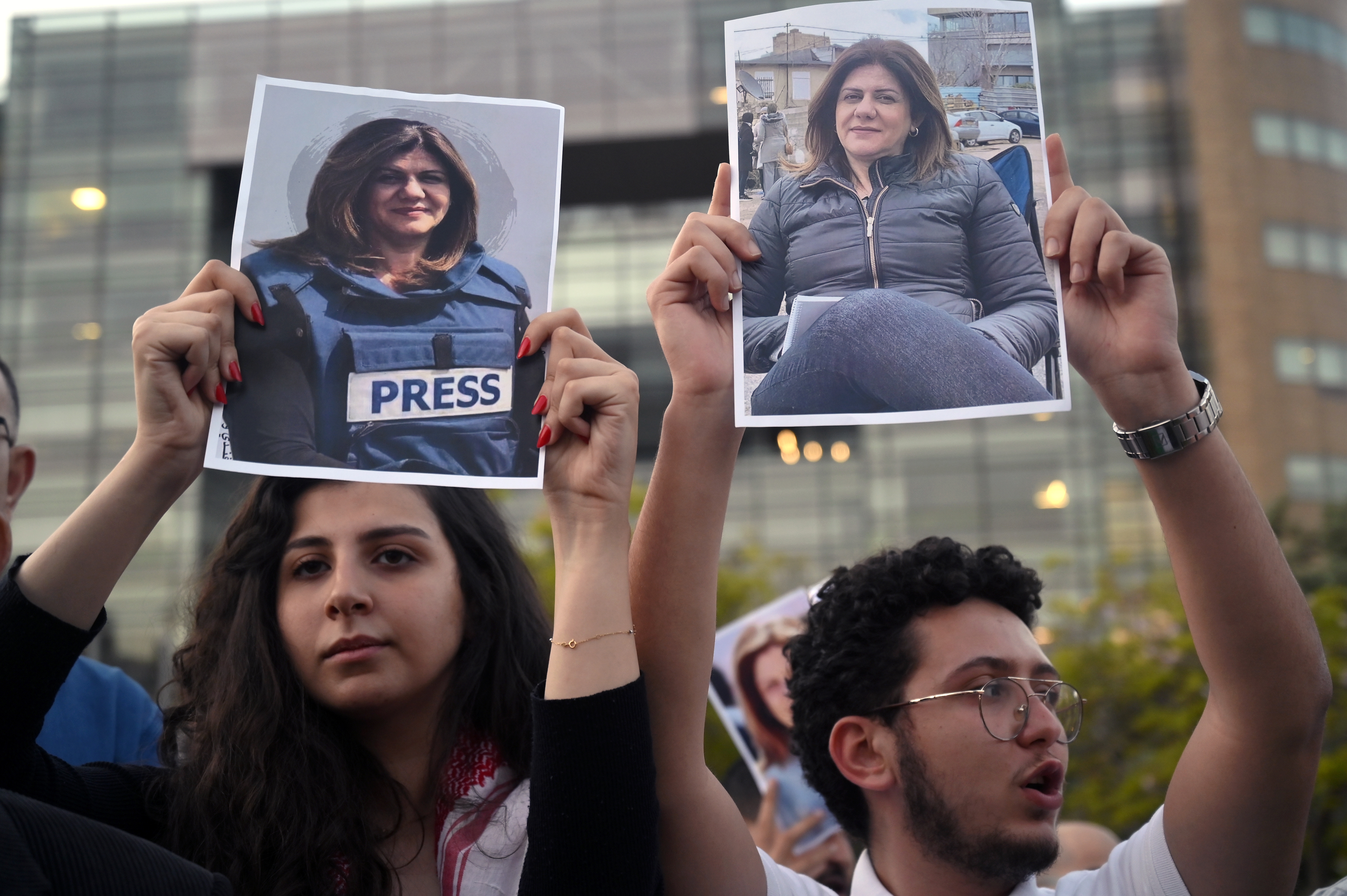 people hold up photos of a woman wearing a press vest at a protest