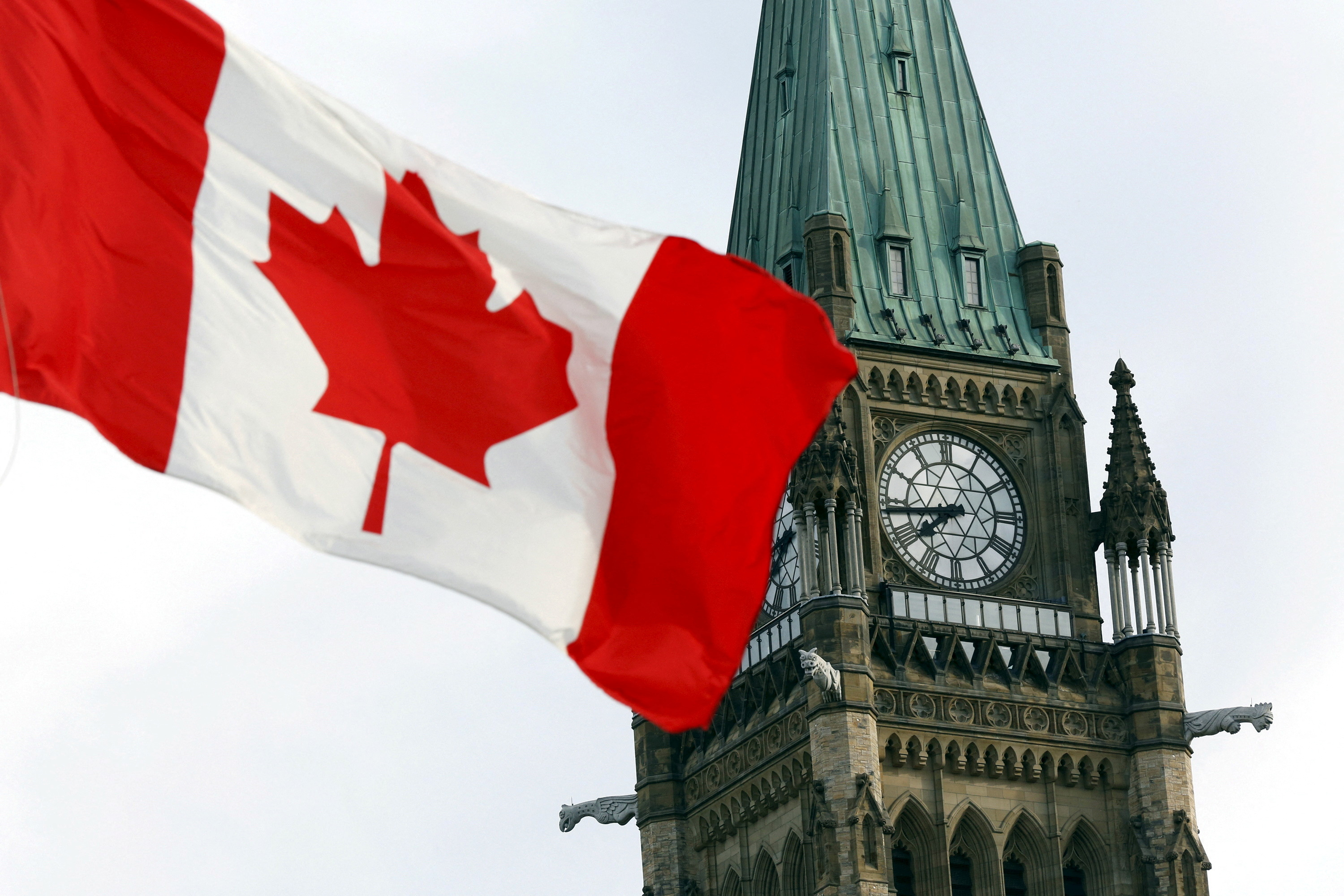 A Canadian flag next to Canada's Parliament building