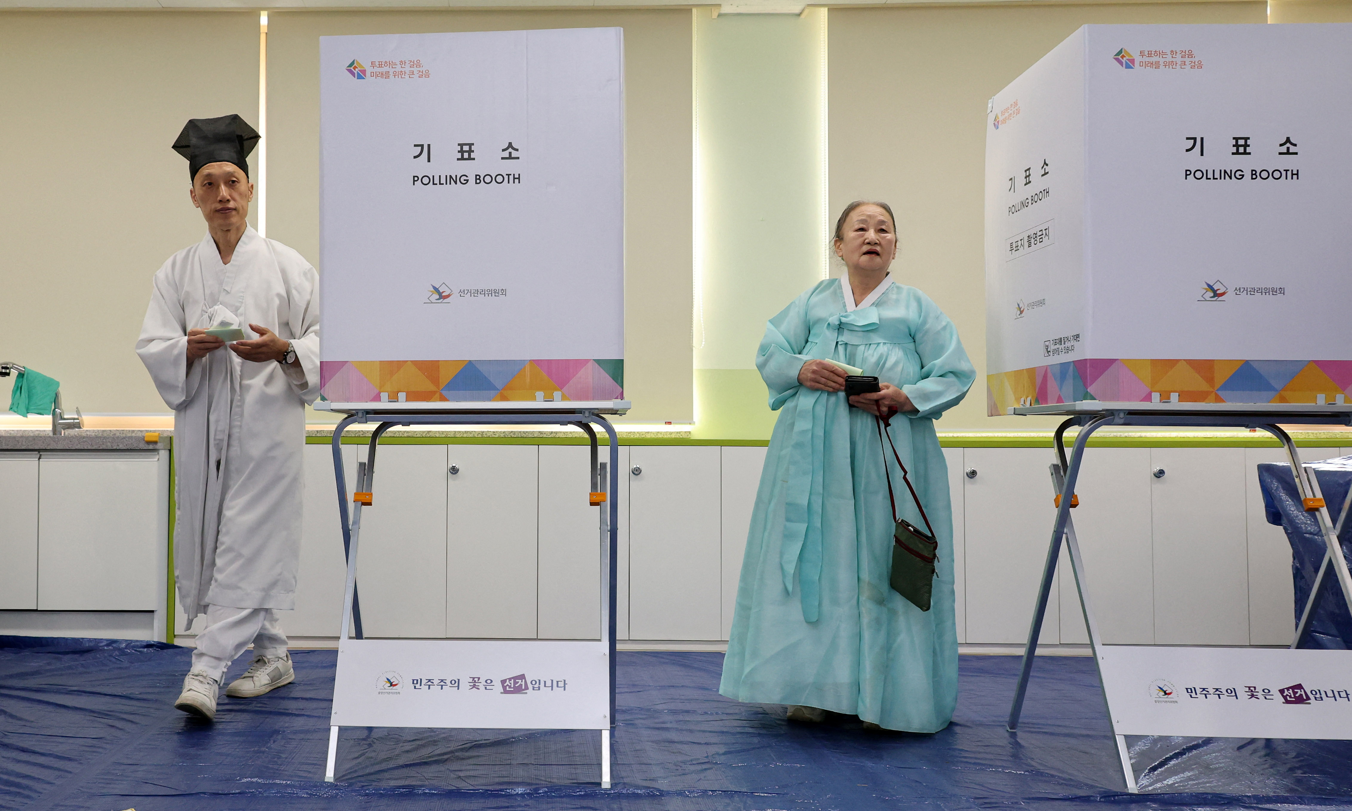 A village schoolmaster and his family in the polling stations. They are wearing traditional dress and standing alongside the polling booths.
