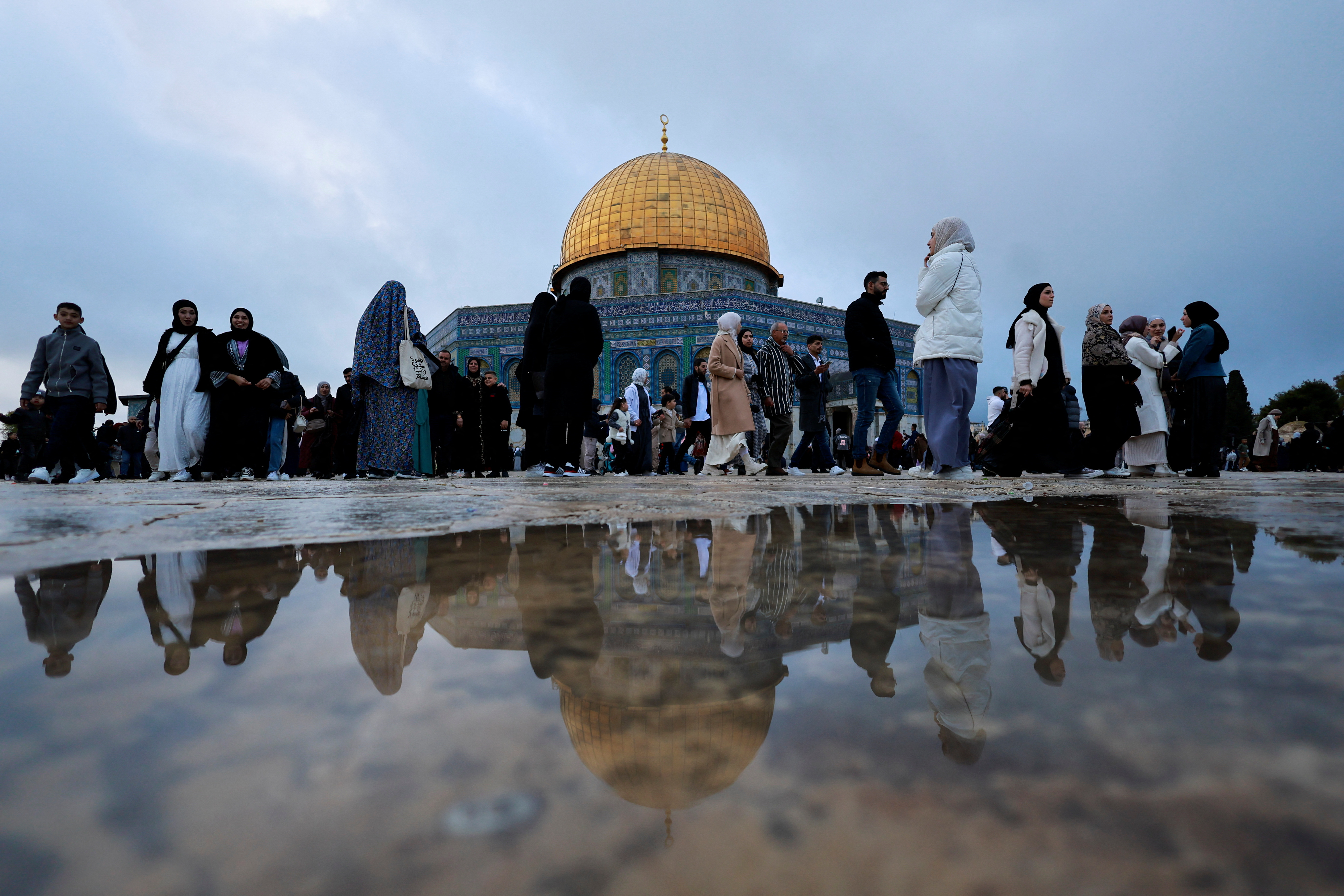 people gather outside a gold domes building with rain on the ground