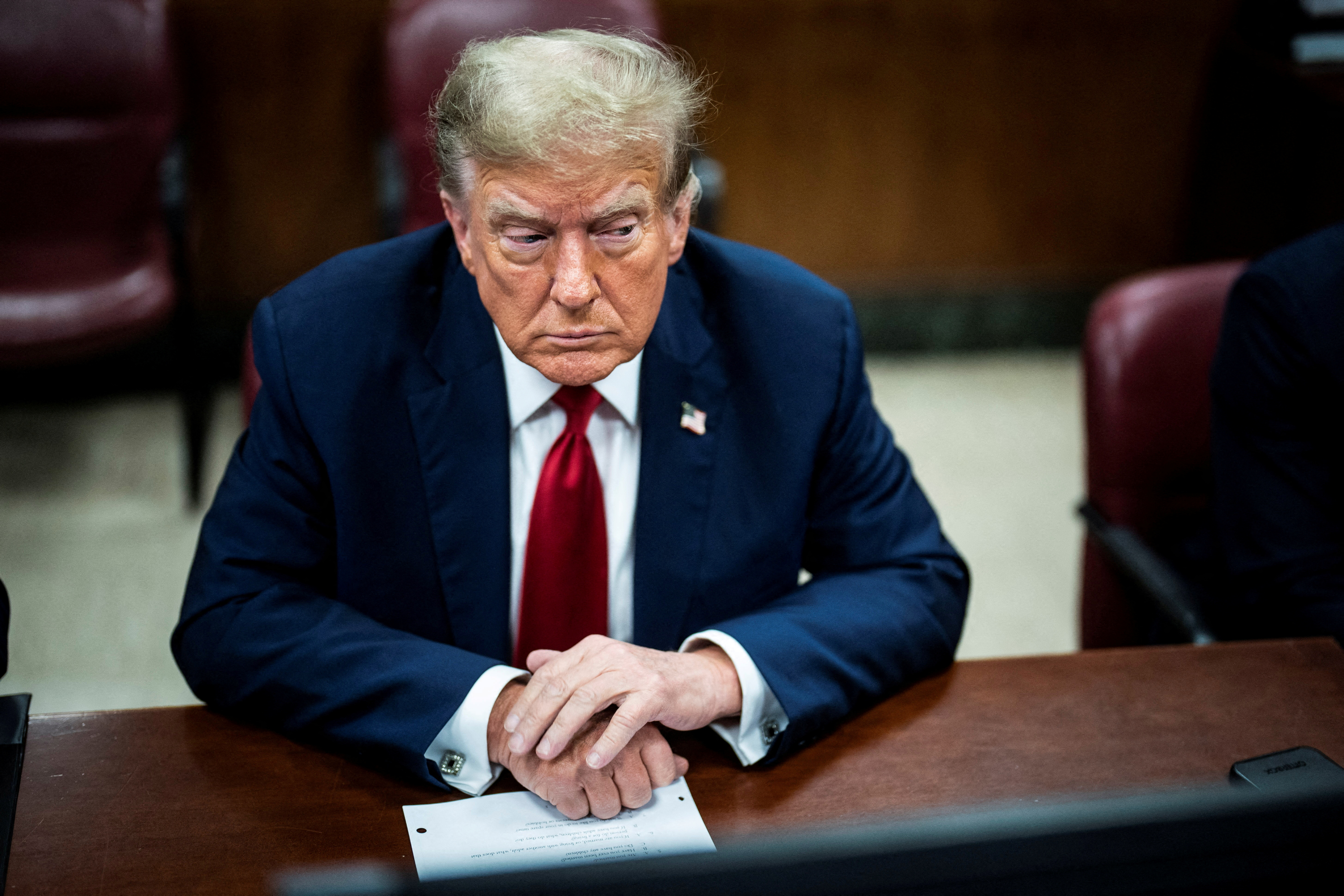 Donald Trump in court. He has his hands clasped over a document on the desk in front of him. He looks serious.