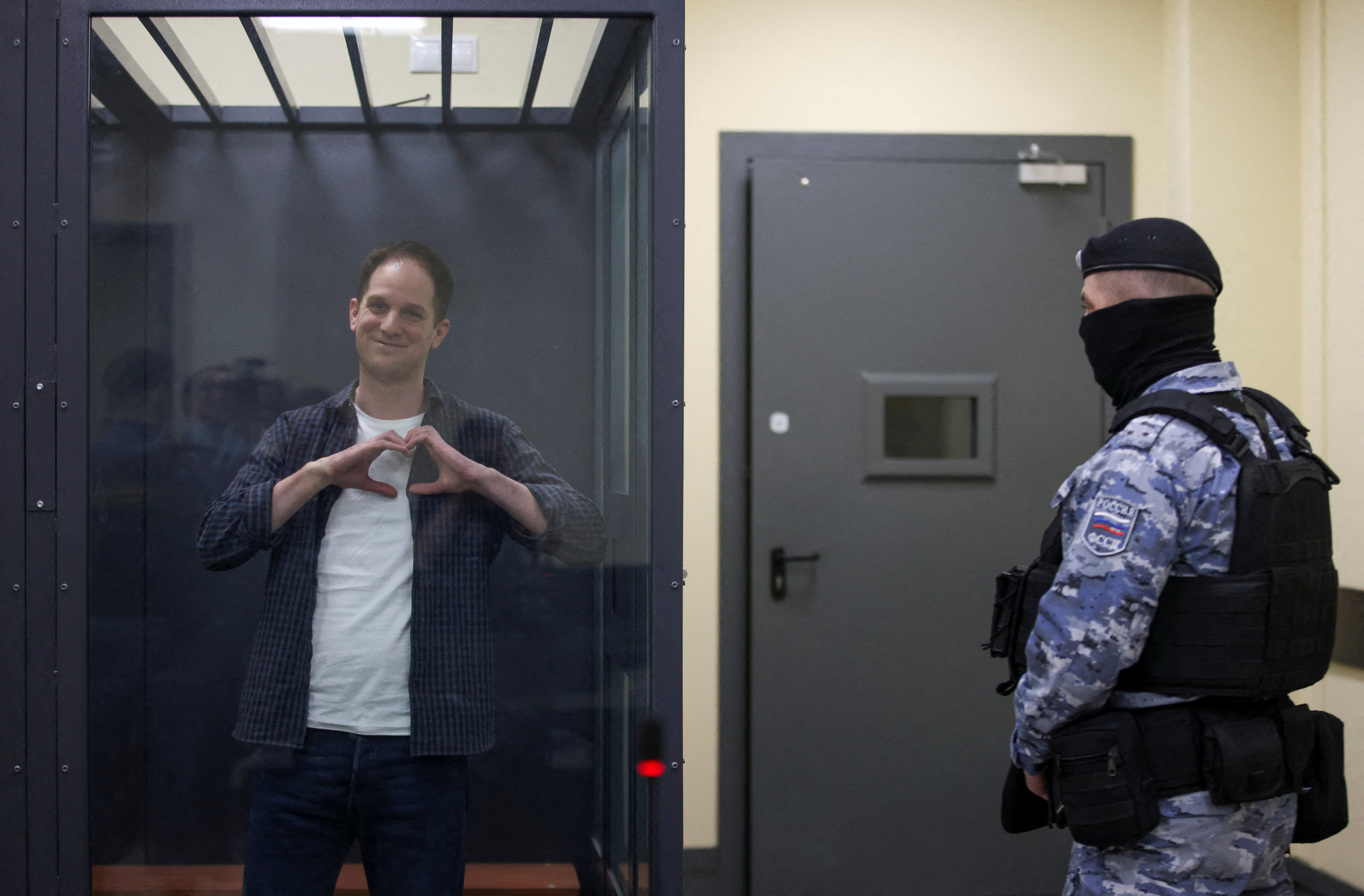 Wall Street Journal reporter Evan Gershkovich, who is in custody on espionage charges, makes a heart-shaped gesture inside an enclosure for defendants before a court hearing in Moscow, Russia, April 23