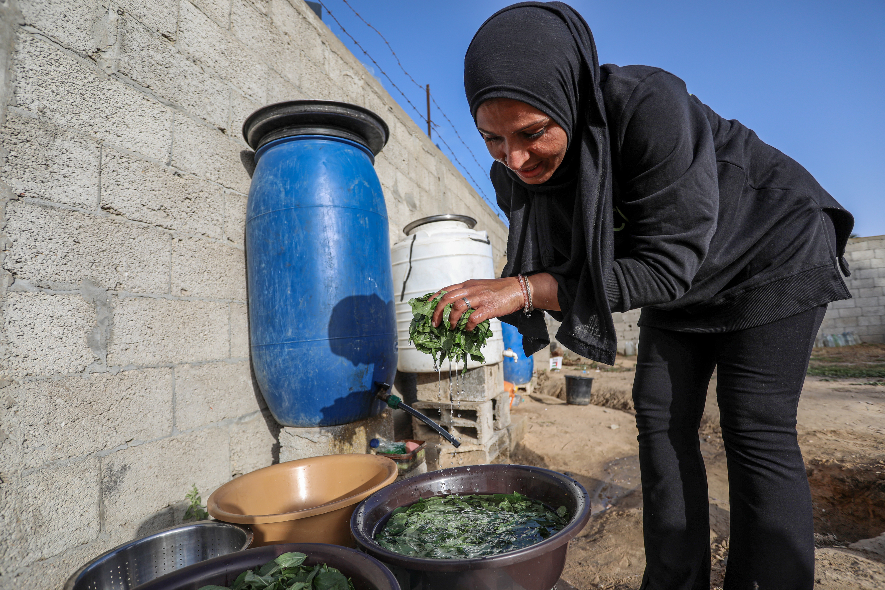 Siham filling a plastic tub with water from a communal tank