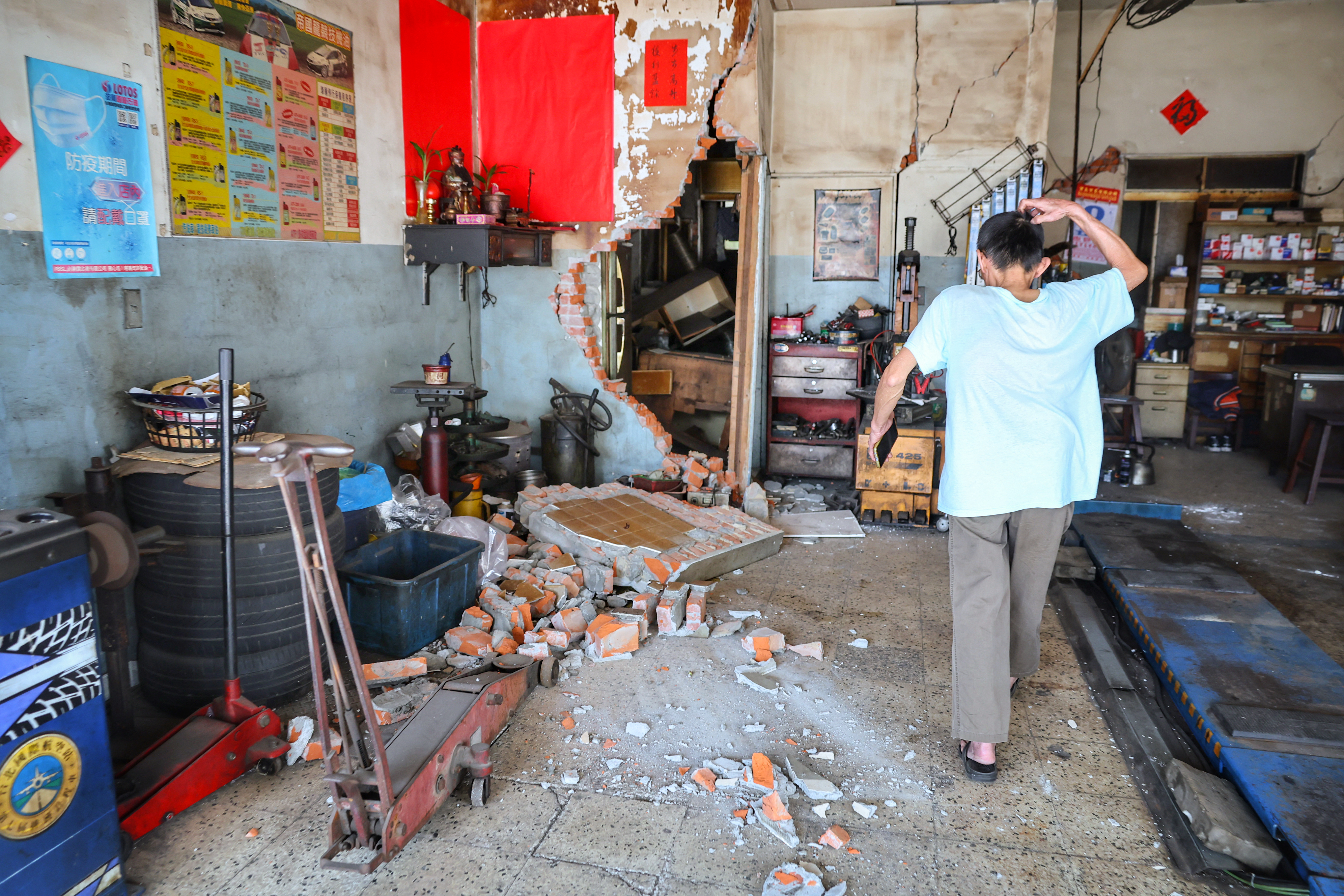 Damage to a house in Taipei where a wall has collapsed. A man is standing inside looking at the debris