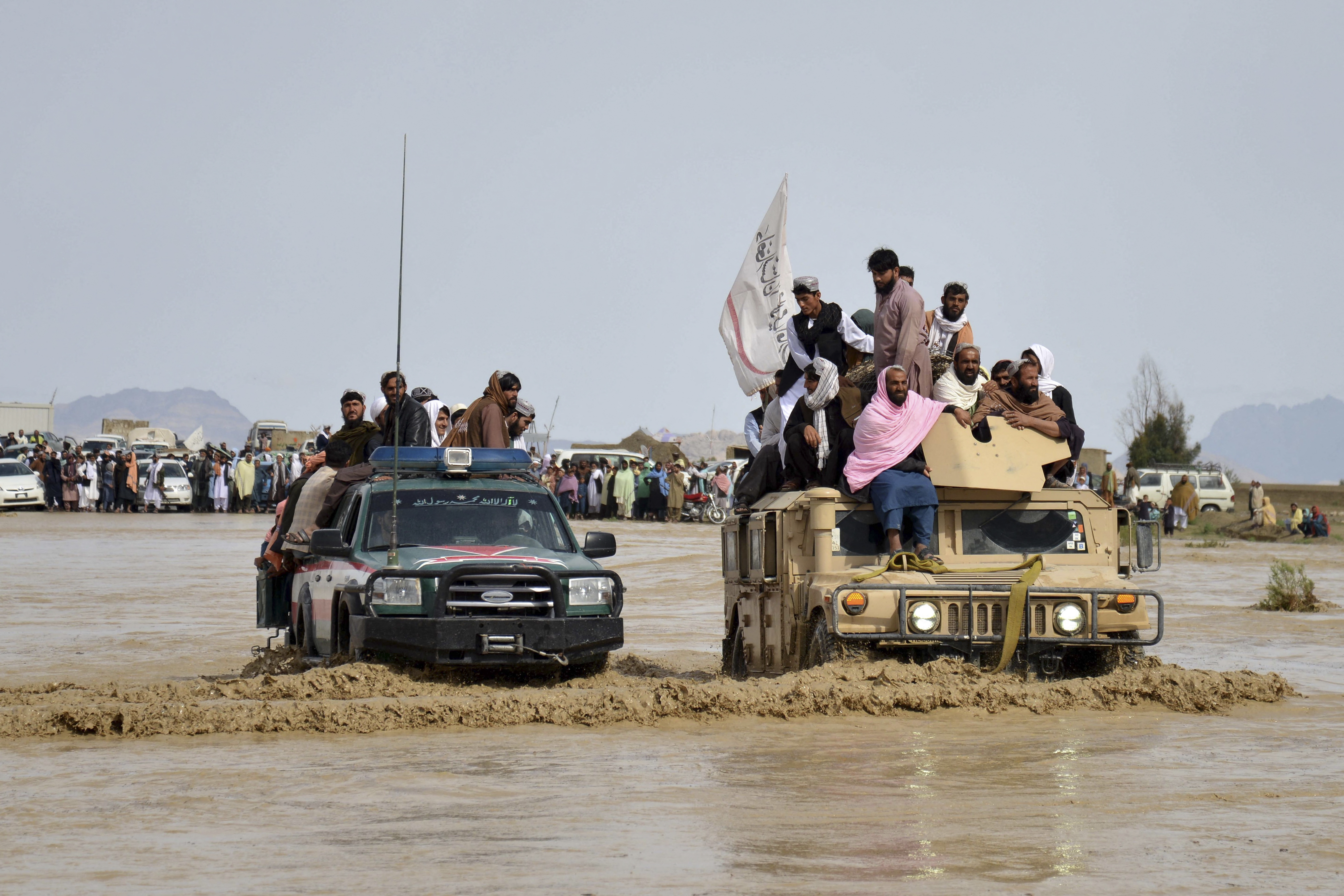 Afghan men sit atop of military vehicles amid flooding