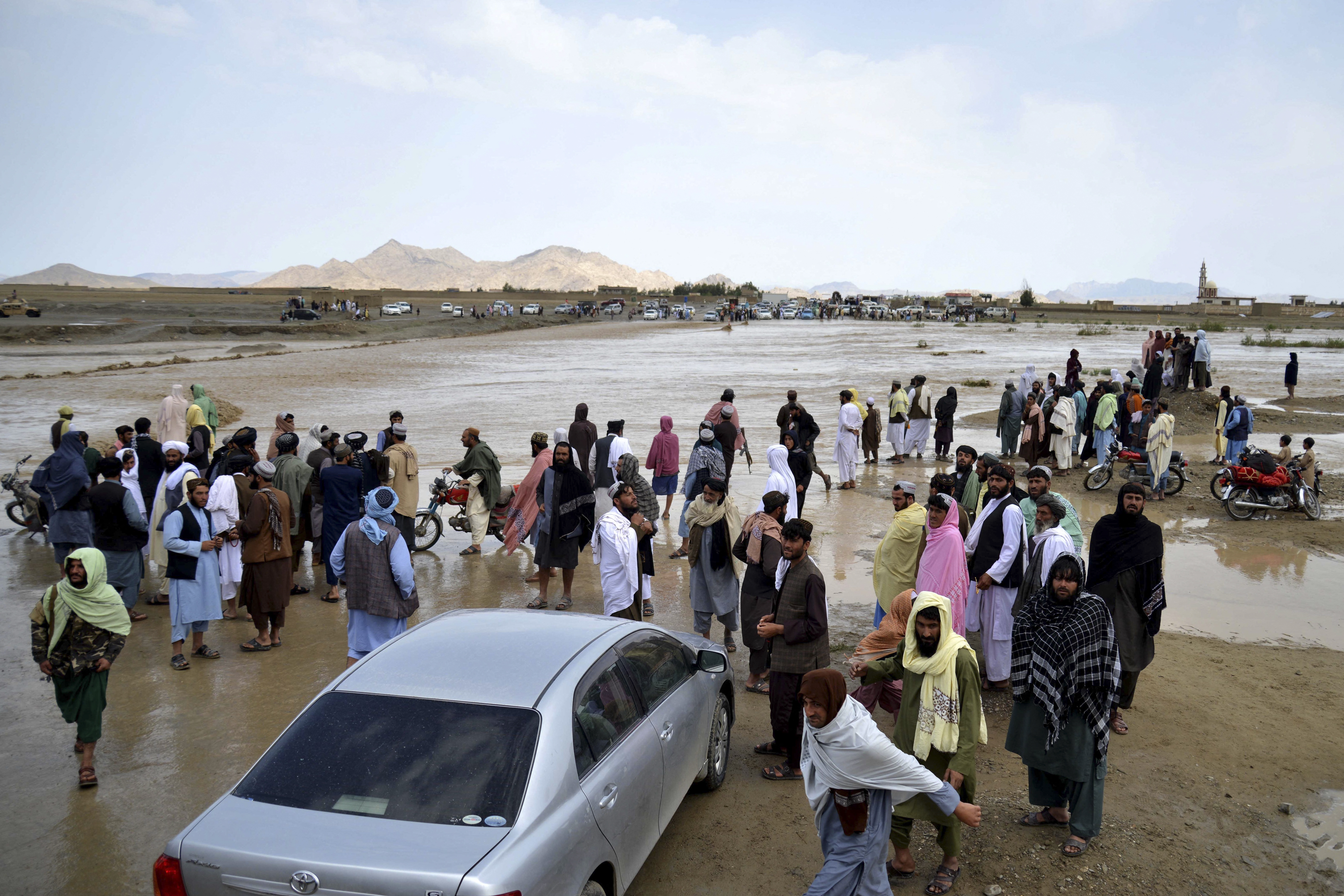 Afghan people wait to cross a flooded area
