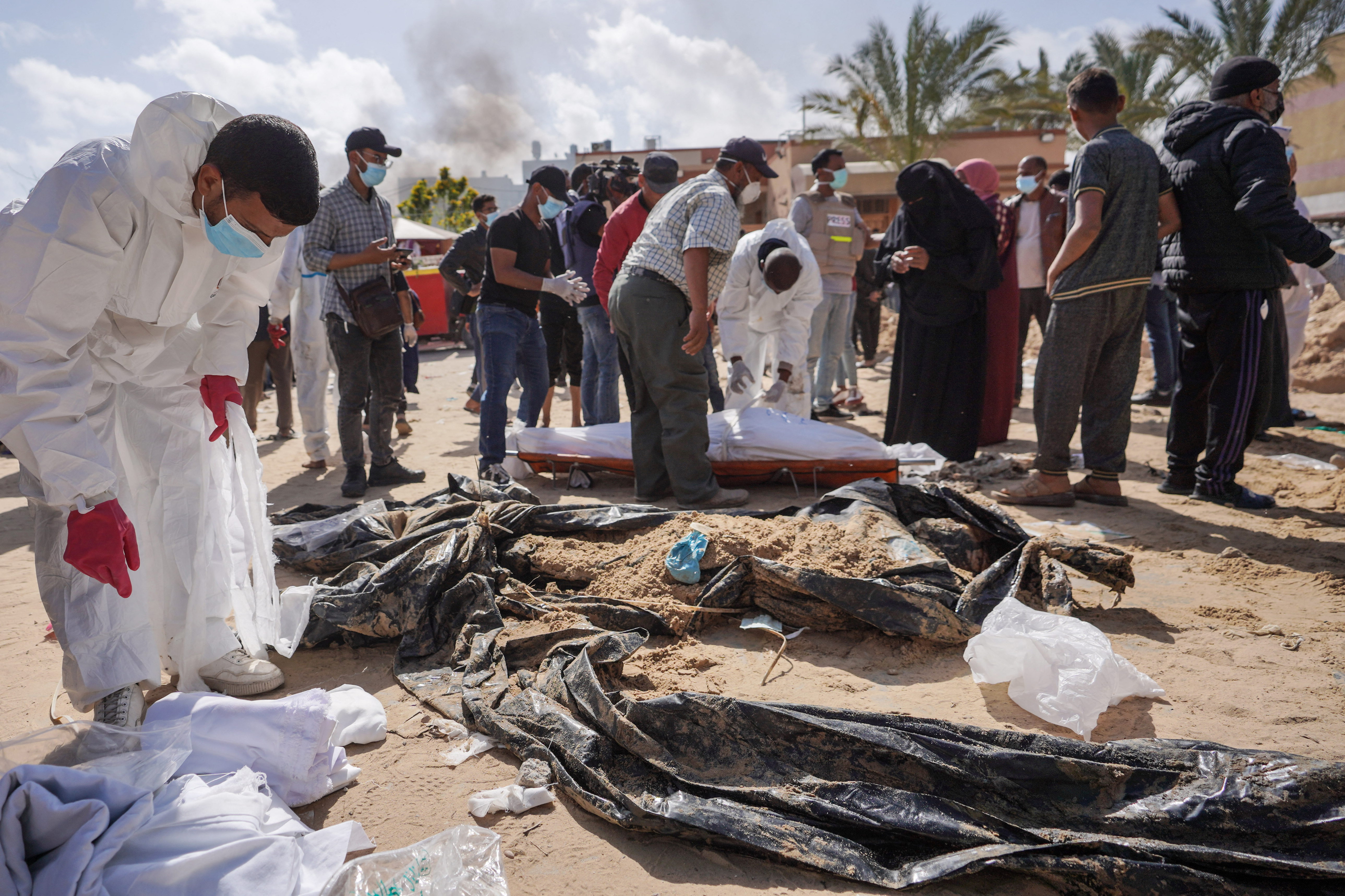 Palestinian health workers stand next to unearthed bodies buried by Israeli forces in Nasser hospital