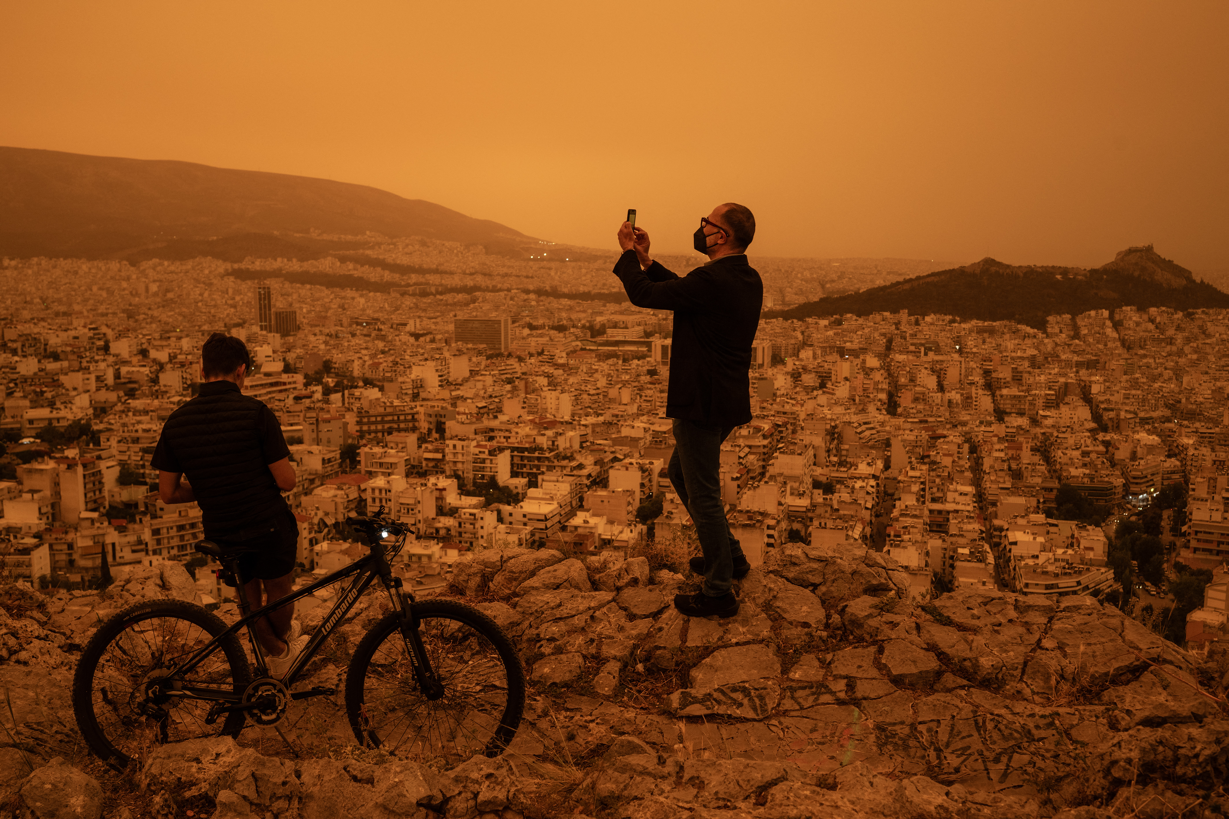 A man takes a photograph of the city of Athens from Tourkovounia hill, as southerly winds carry waves of Saharan dust to the city, in Athens, on April 23