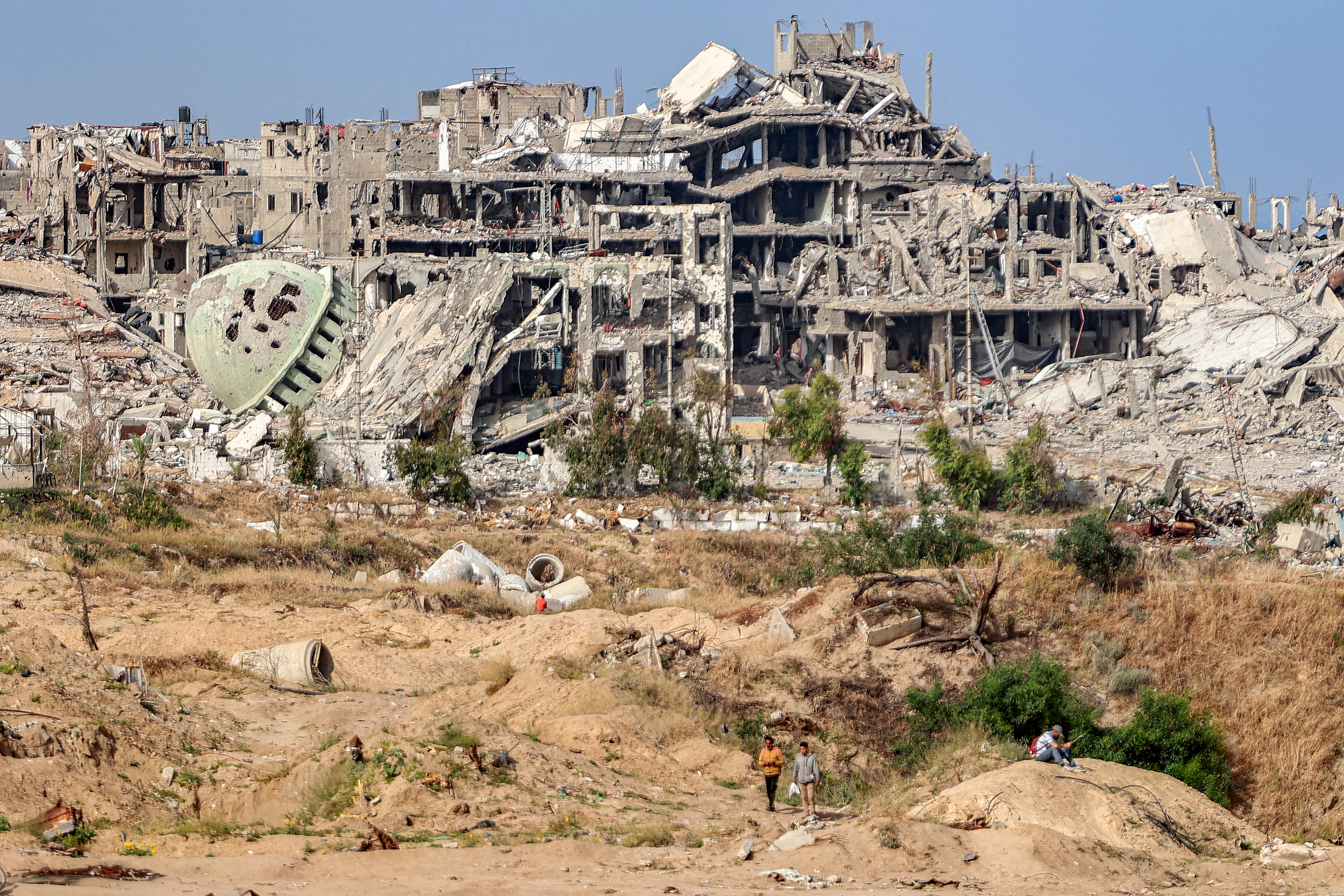People wait before destroyed buildings in cleared area by the coastline for humanitarian aid packages to drop over the northern Gaza Strip