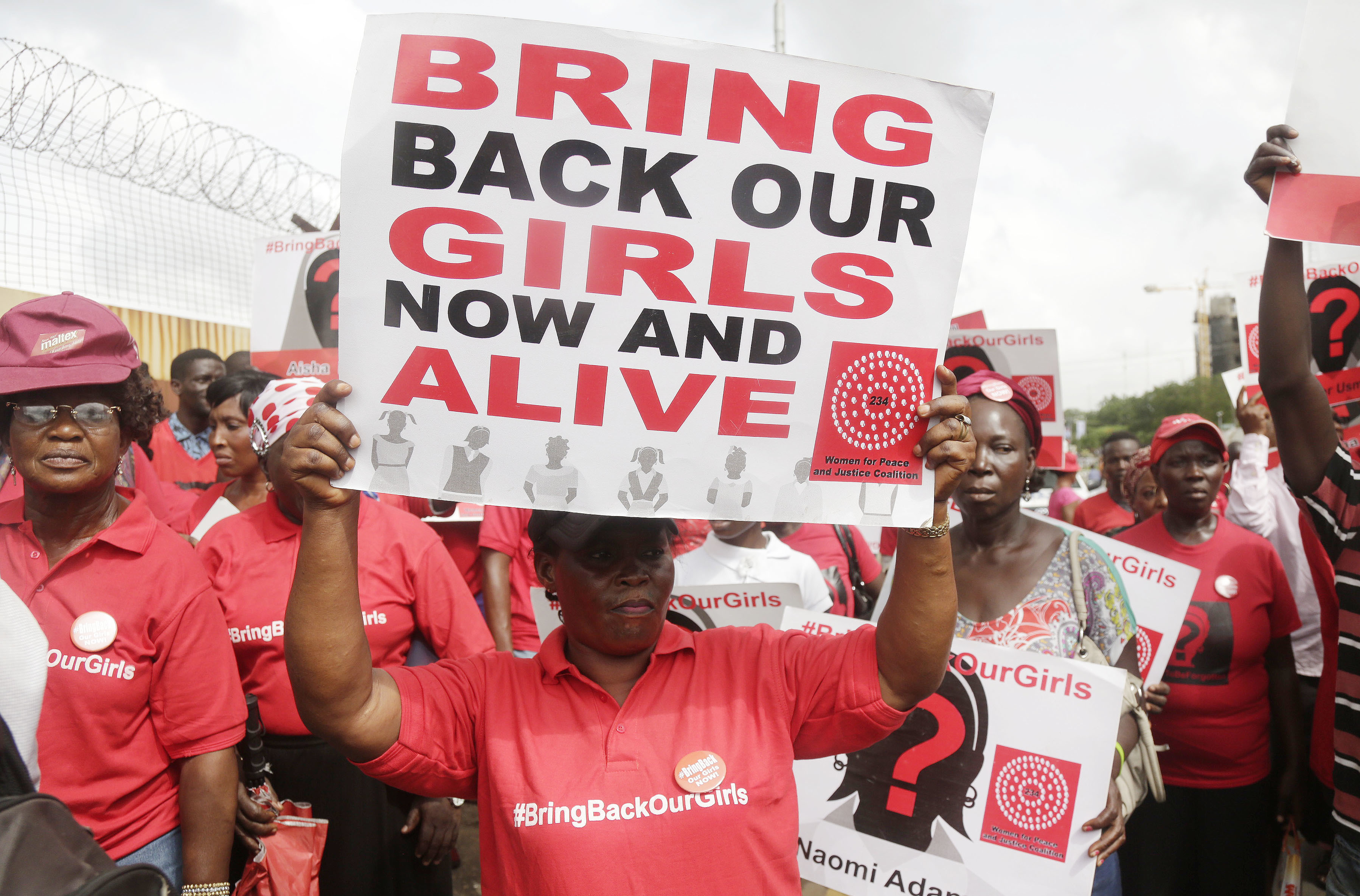 A person holds a sign that says 'Bring back our girls now and alive'