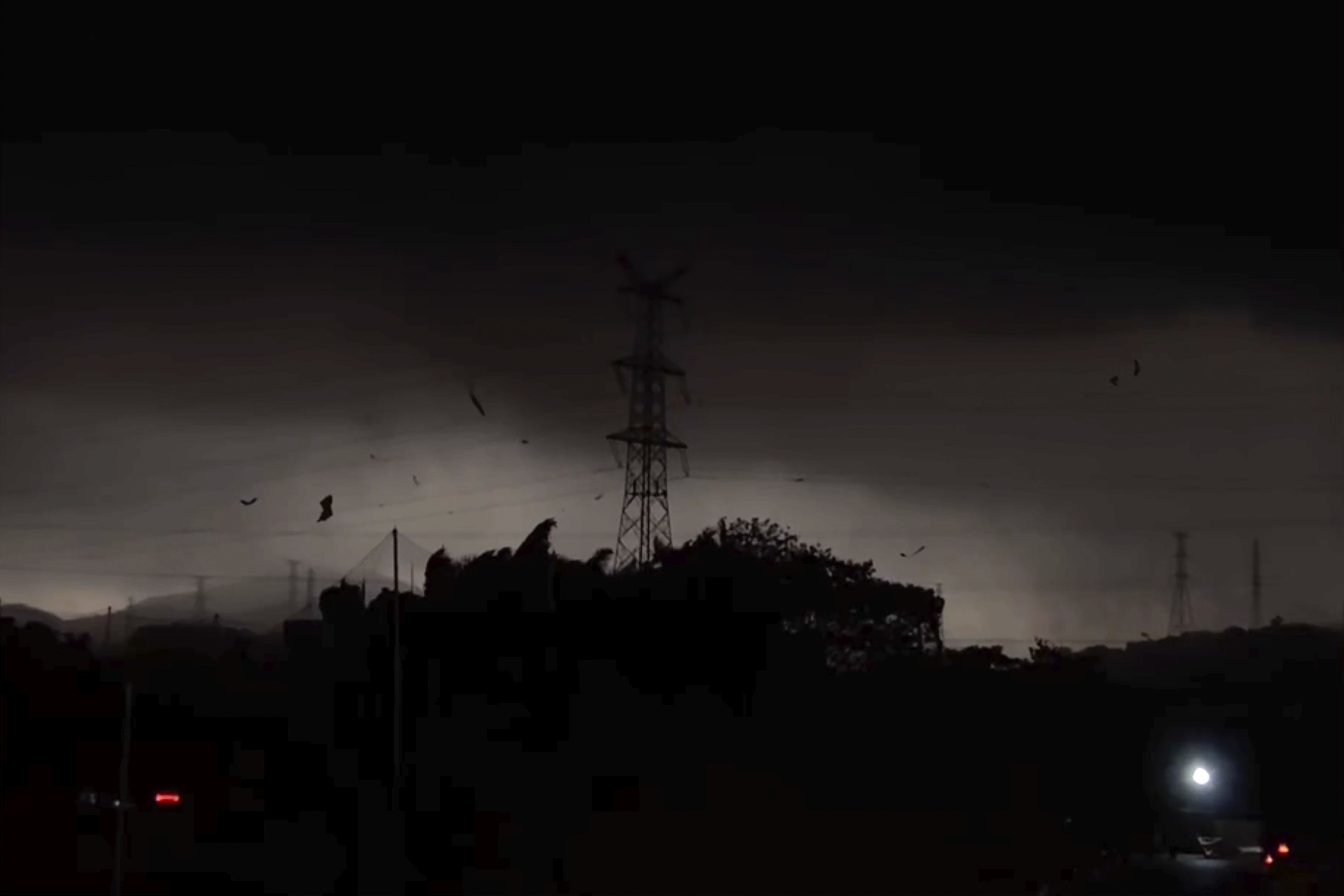 The storm over the Baiyun district. The sky is almost black and an electricity pylon is silhouetted against the lighter clouds.. There is debris being blown about by the wind.