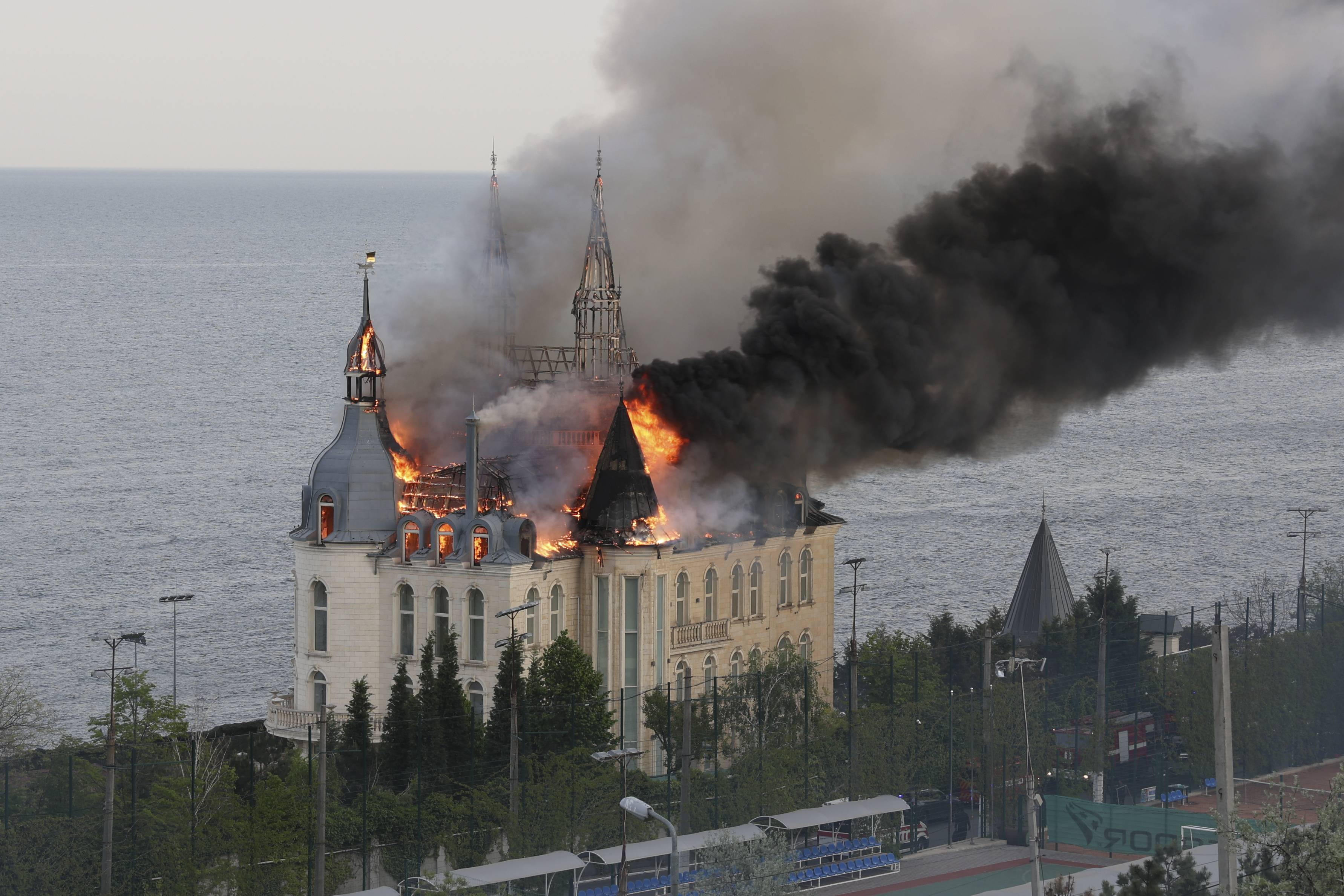 Black smoke and flames billow from the Odesa Law Academy. The building is ornate. The sea is next to the building.