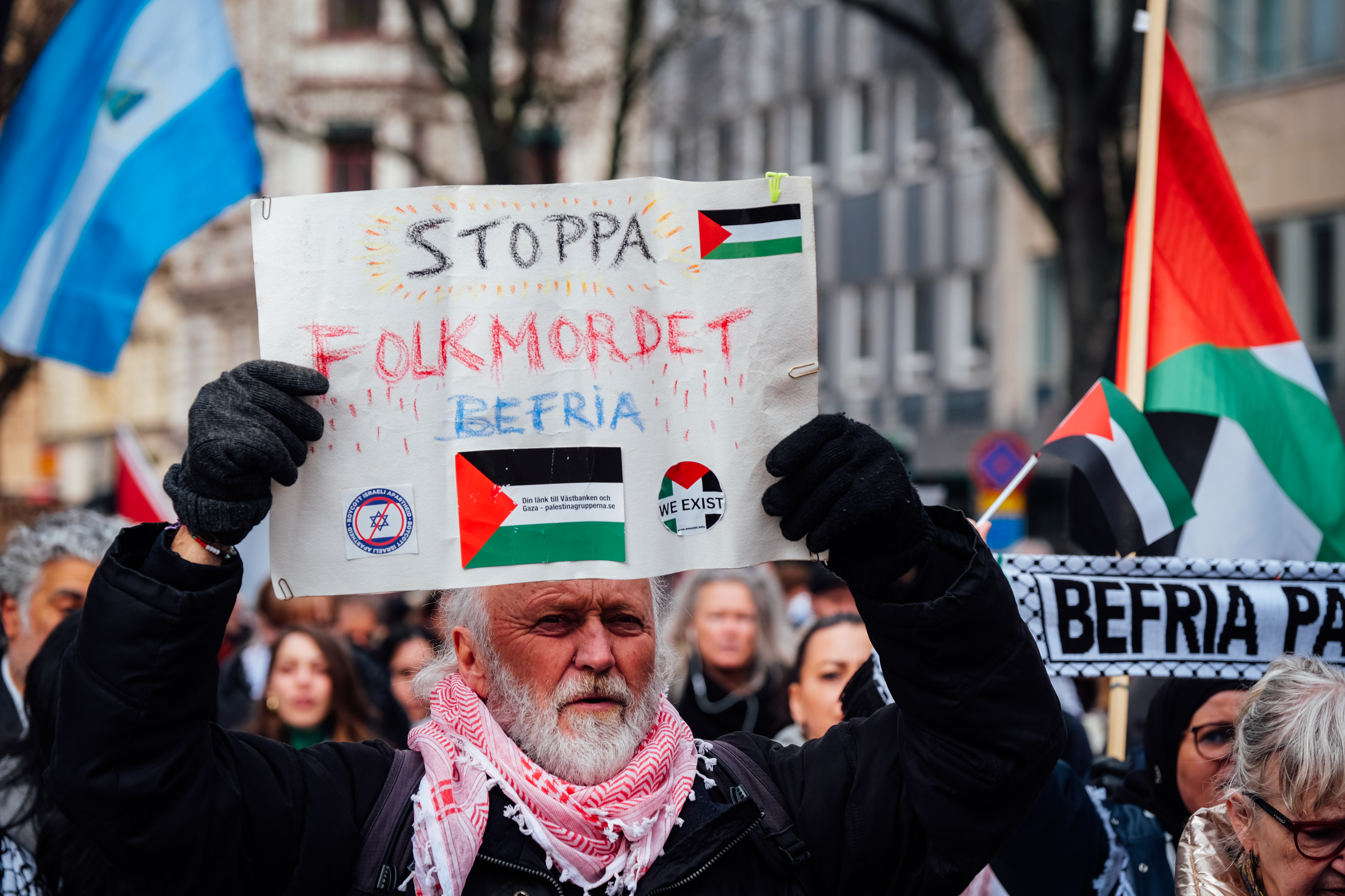 A man wears a Palestinian keffiyeh and holds up a banner in a protest.