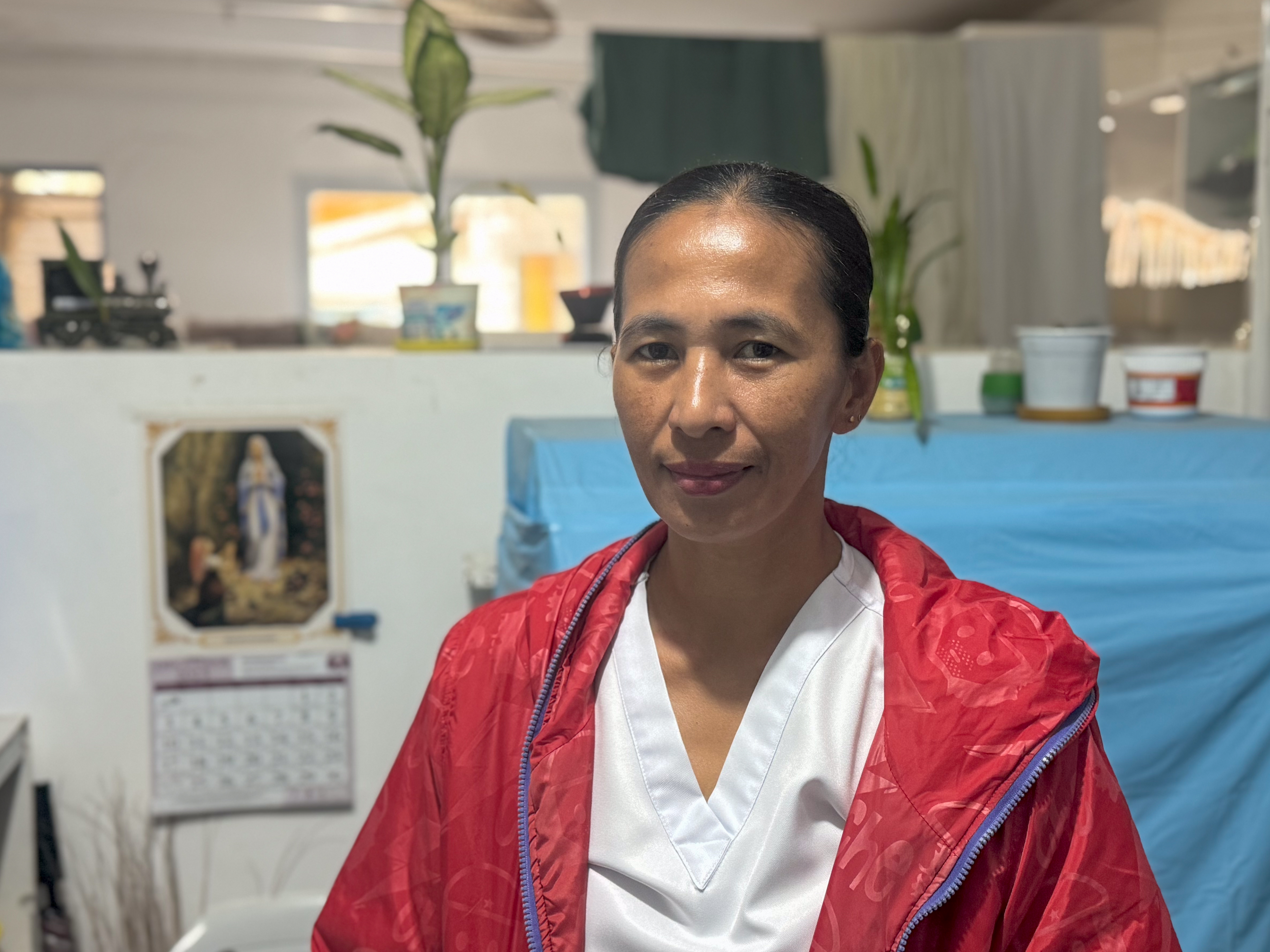 Sheila Manzano, a nurse practitioner. She is wearing her uniform with a red jacket. She is seated inside.