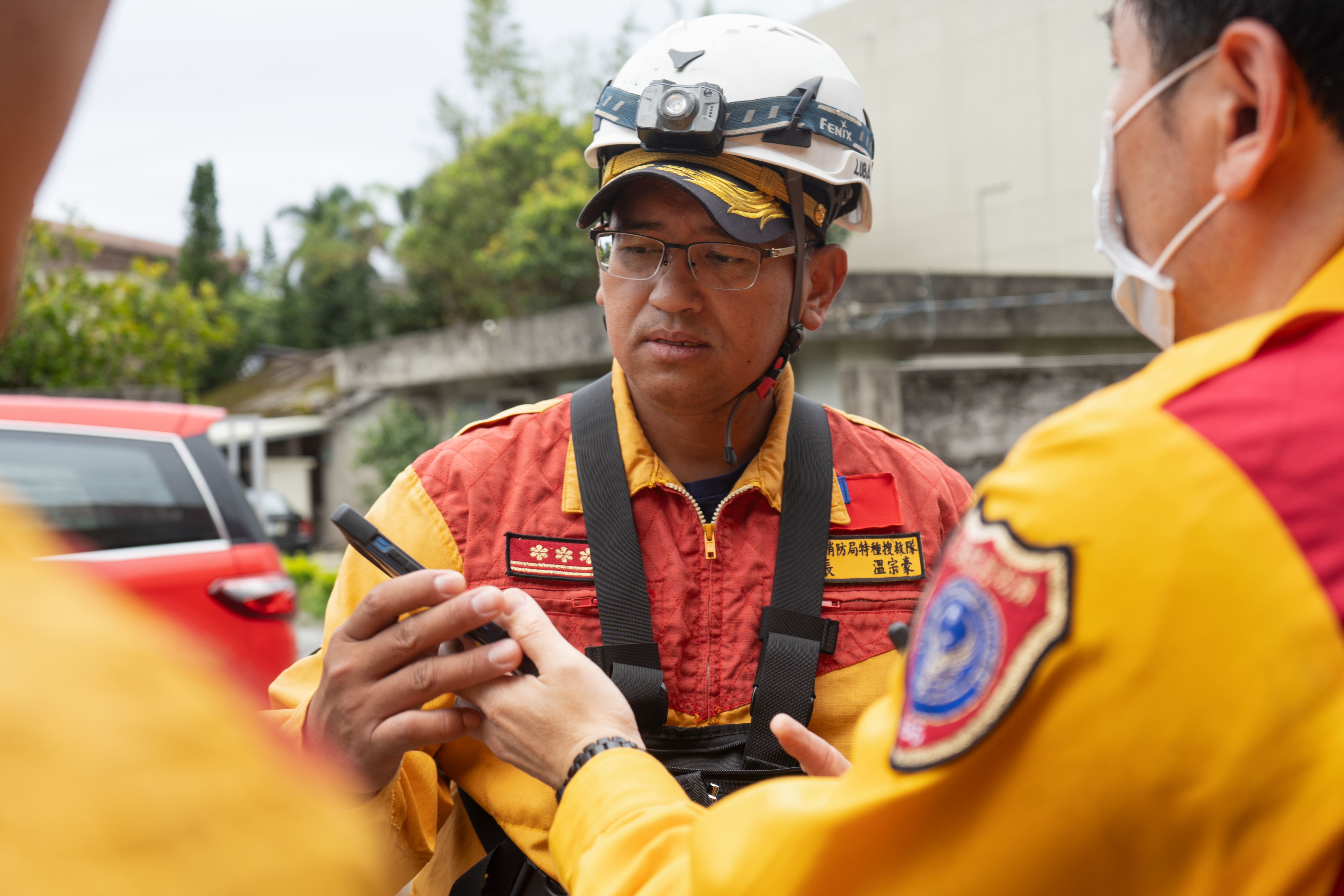 Wen Zong Hao. He is looking at a mobile phone being shared by a colleague. They are in orange and yellow unifirms and wearing hard hats.