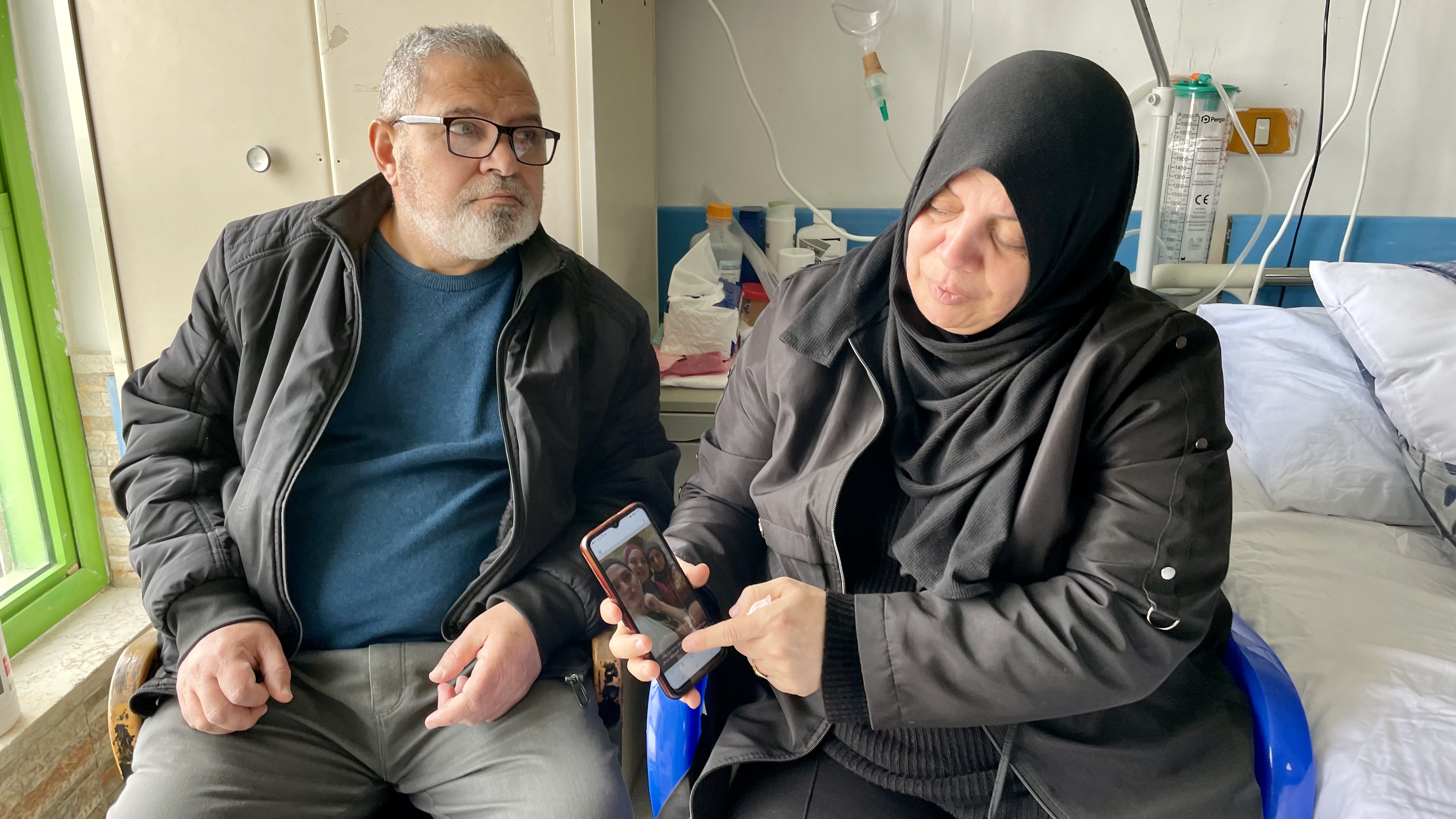 Hanan and Mazen in hospital room, Hanan showing photos of kids on the phone