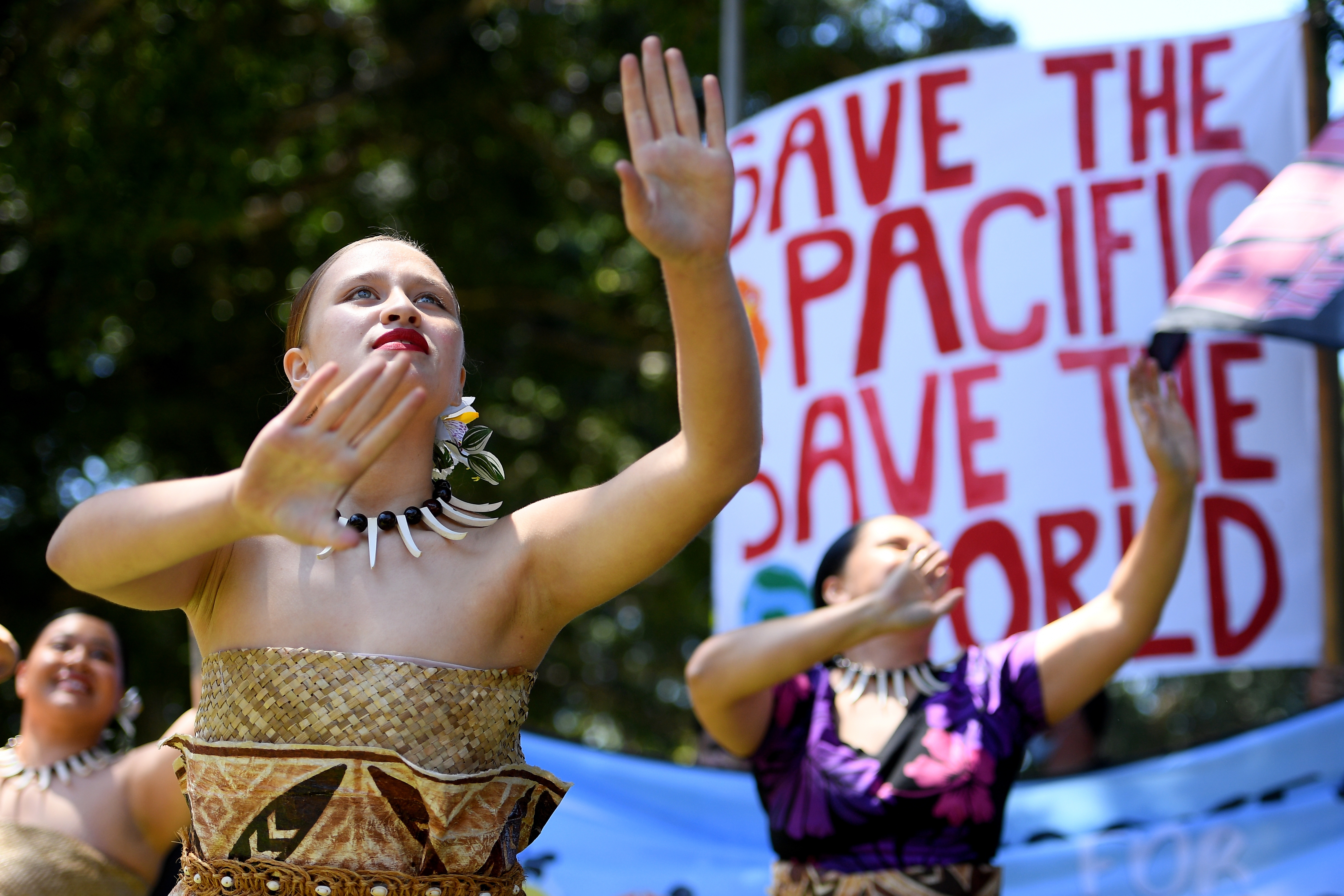 people dance in front of a banner that says save the pacific save the world