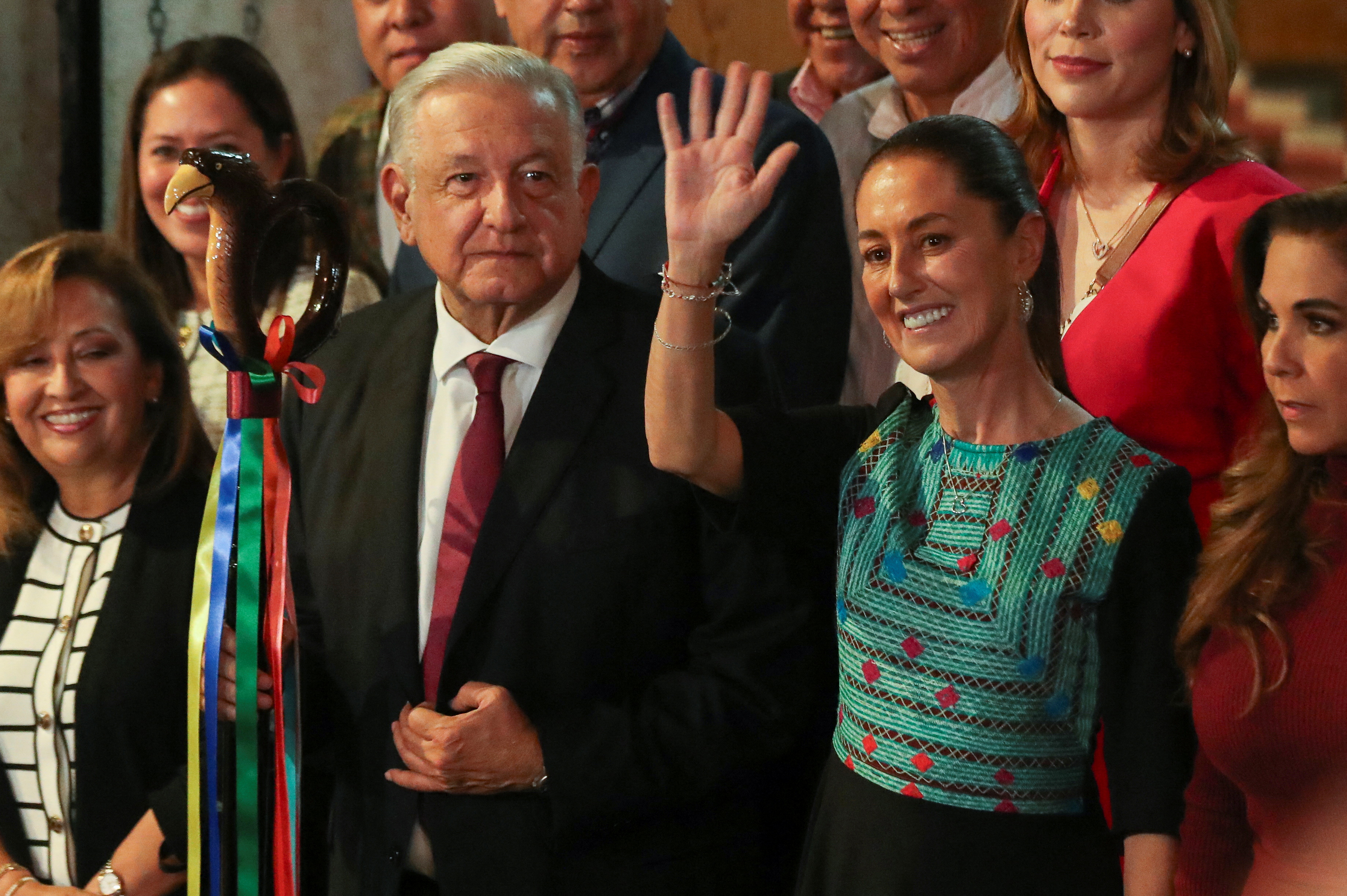 Andres Manuel Lopez Obrador stands next to Claudia Sheinbaum, who waves.