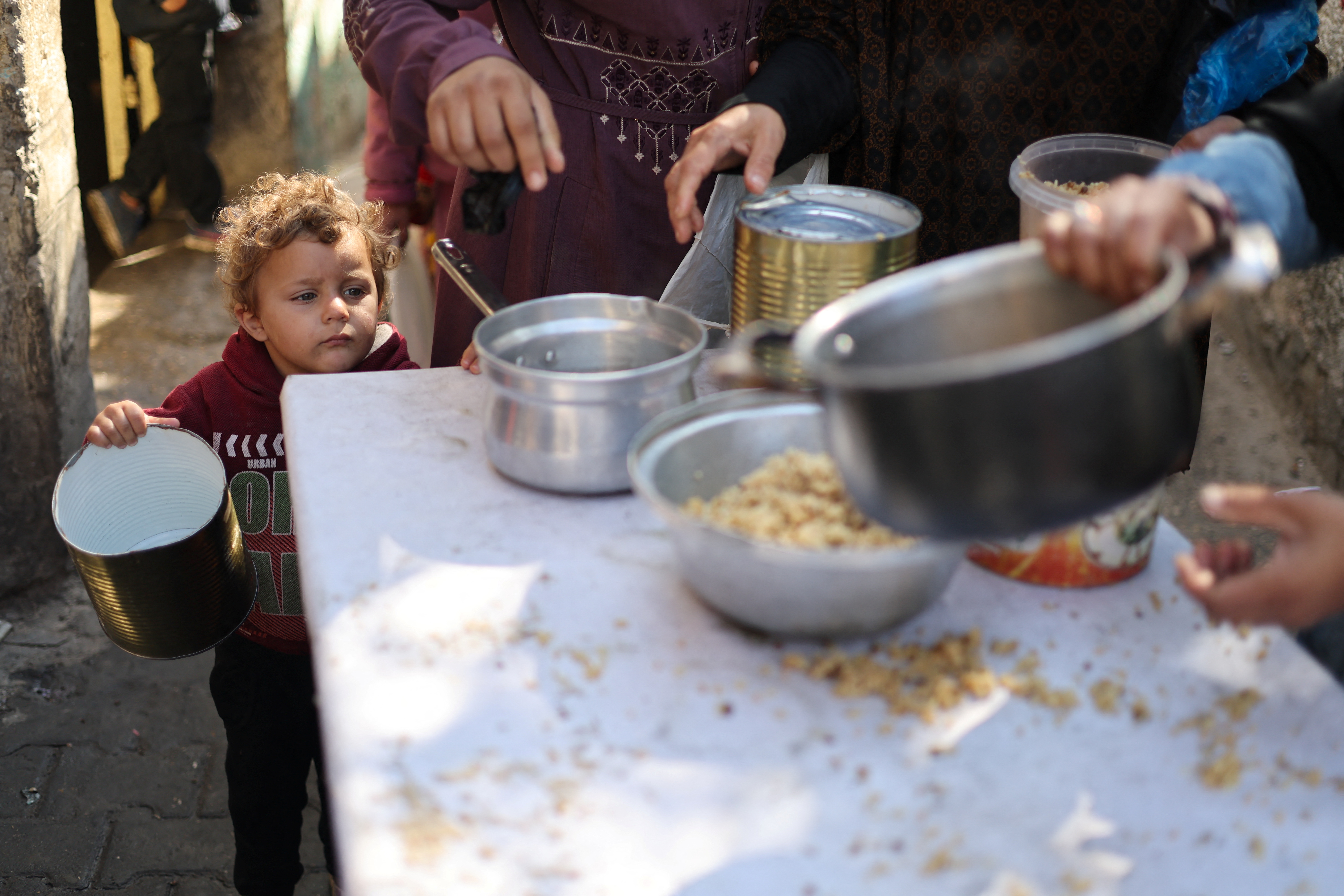 A Palestinian child waits to receive food cooked by a charity kitchen amid shortages of food supplies, as the ongoing conflict between Israel and the Palestinian Islamist group Hamas continues, in Rafah, in the southern Gaza Strip