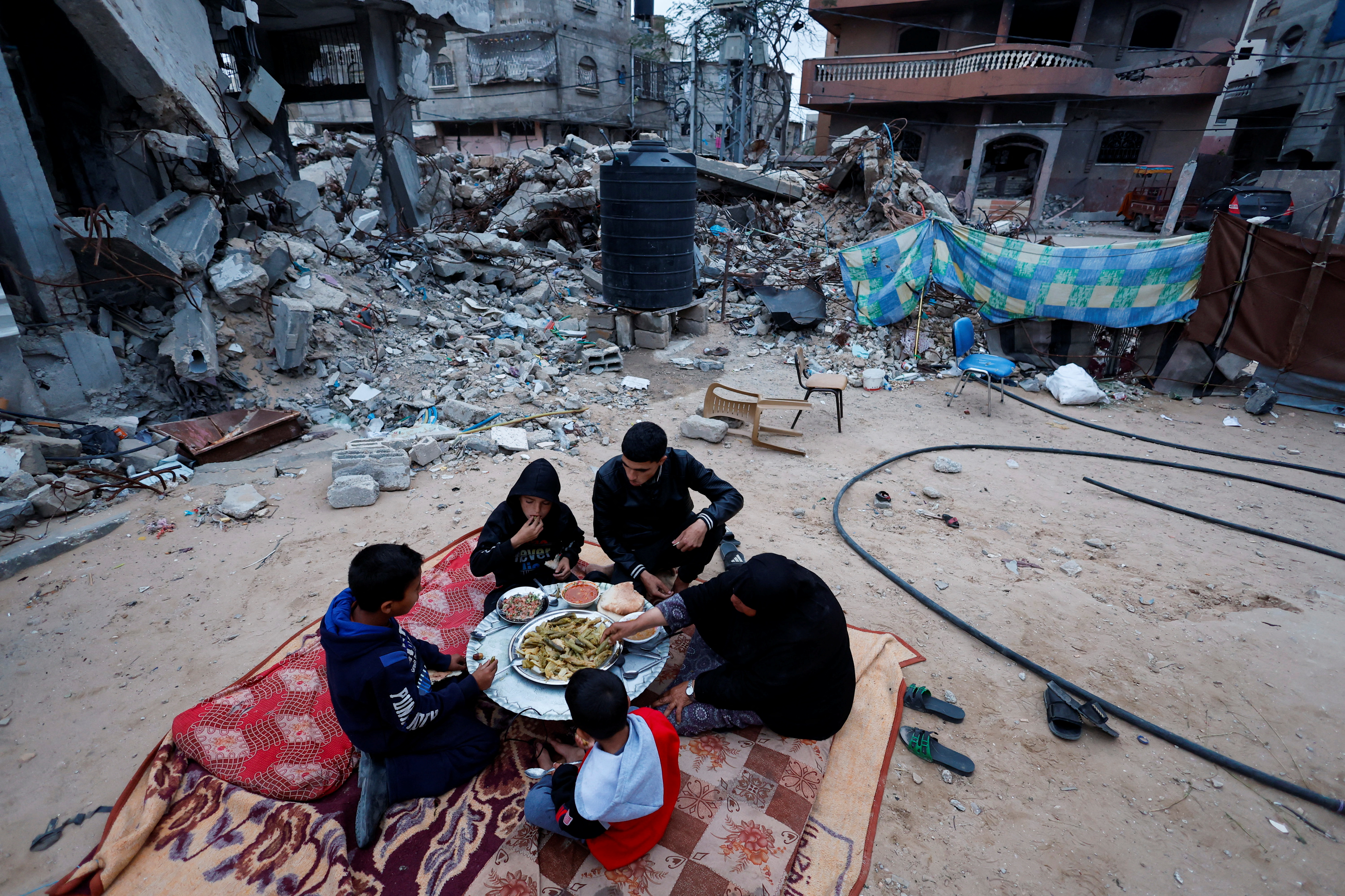 Members of Palestinian Abu Ghouta family eat their iftar meal as they break their fast near the rubble of their destroyed house during the holy month of Ramadan, amid the ongoing conflict between Israel and Hamas, in Rafah in the southern Gaza Strip, March 21, 2024. REUTERS/Mohammed Salem