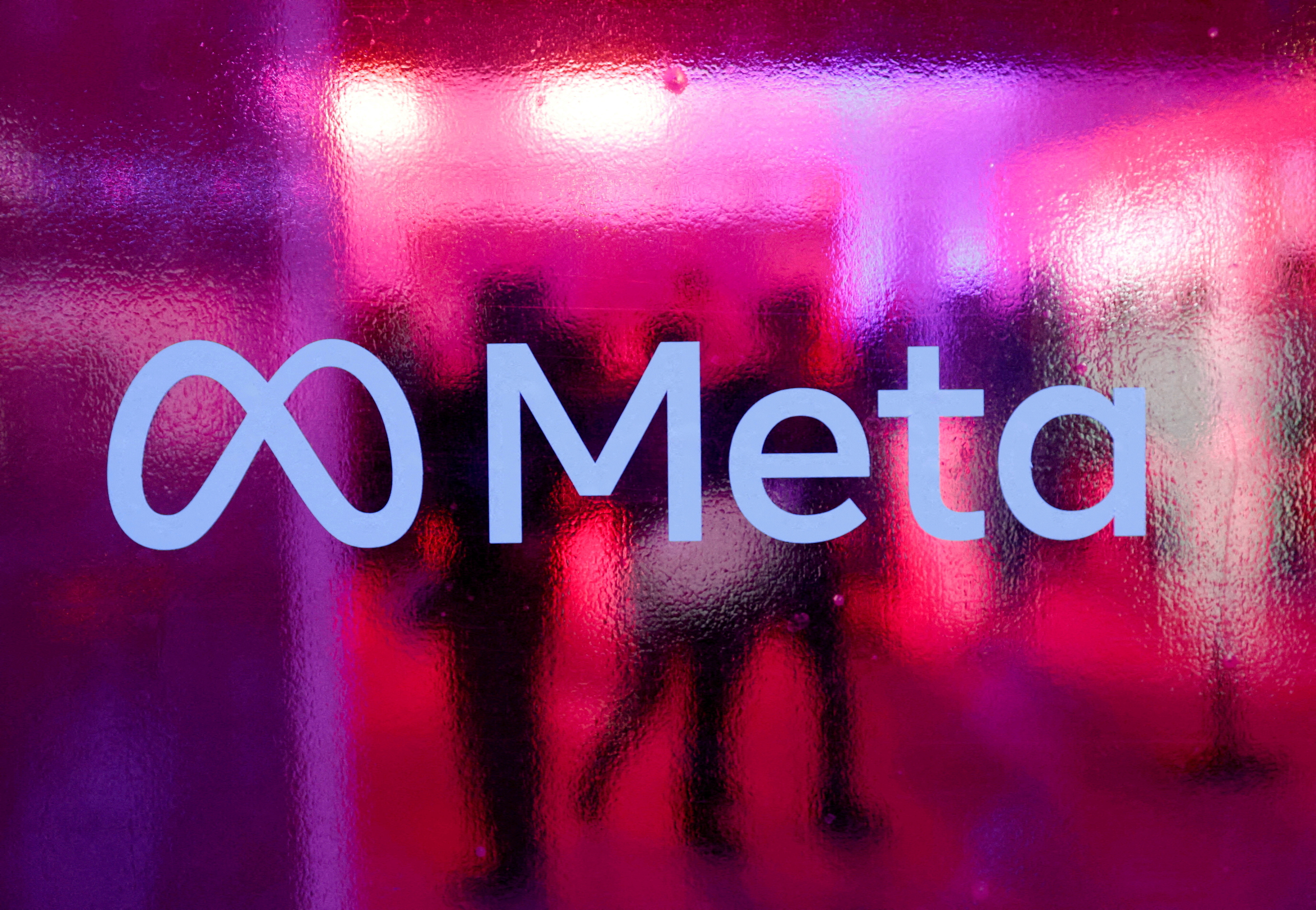 People walk behind a Meta Platforms logo