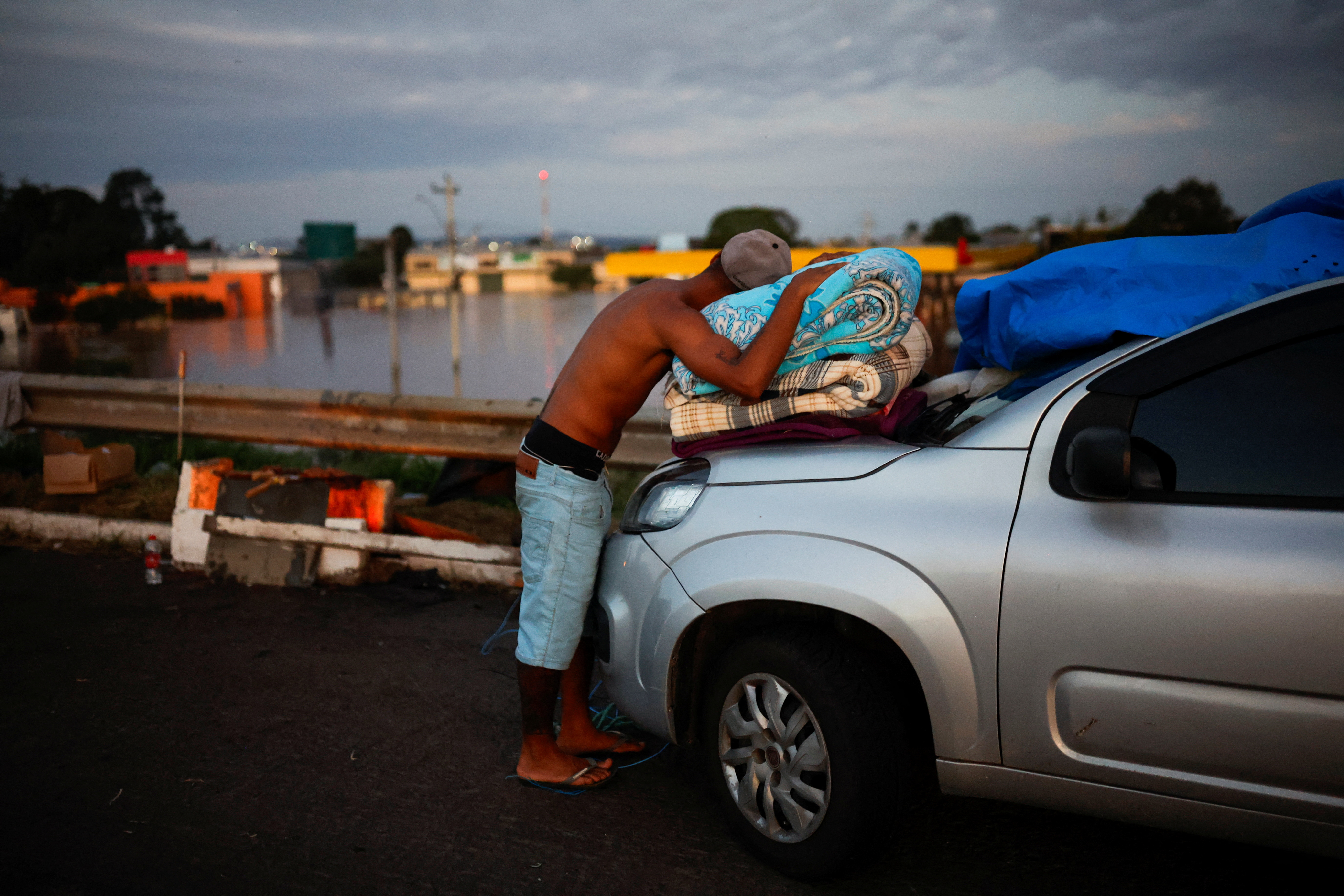 A man leans on blankets near a flooded street in Brazil
