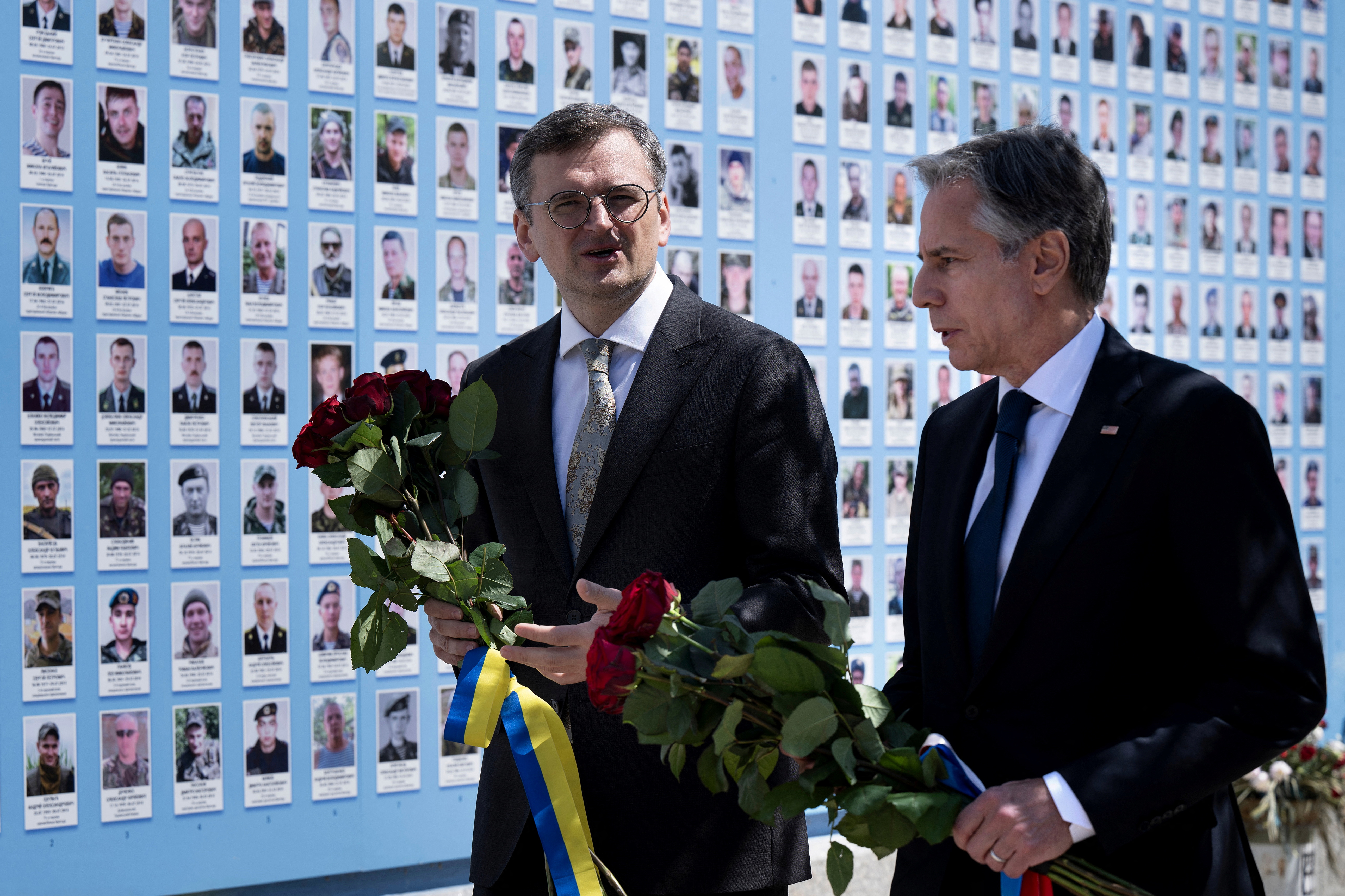 Ukraine's Foreign Minister Dmytro Kuleba and U.S. Secretary of State Antony Blinken walk holding bunches of red roses past the Memory Wall of Fallen Defenders of Ukraine outside the Saint Michael's Cathedral in Kyiv