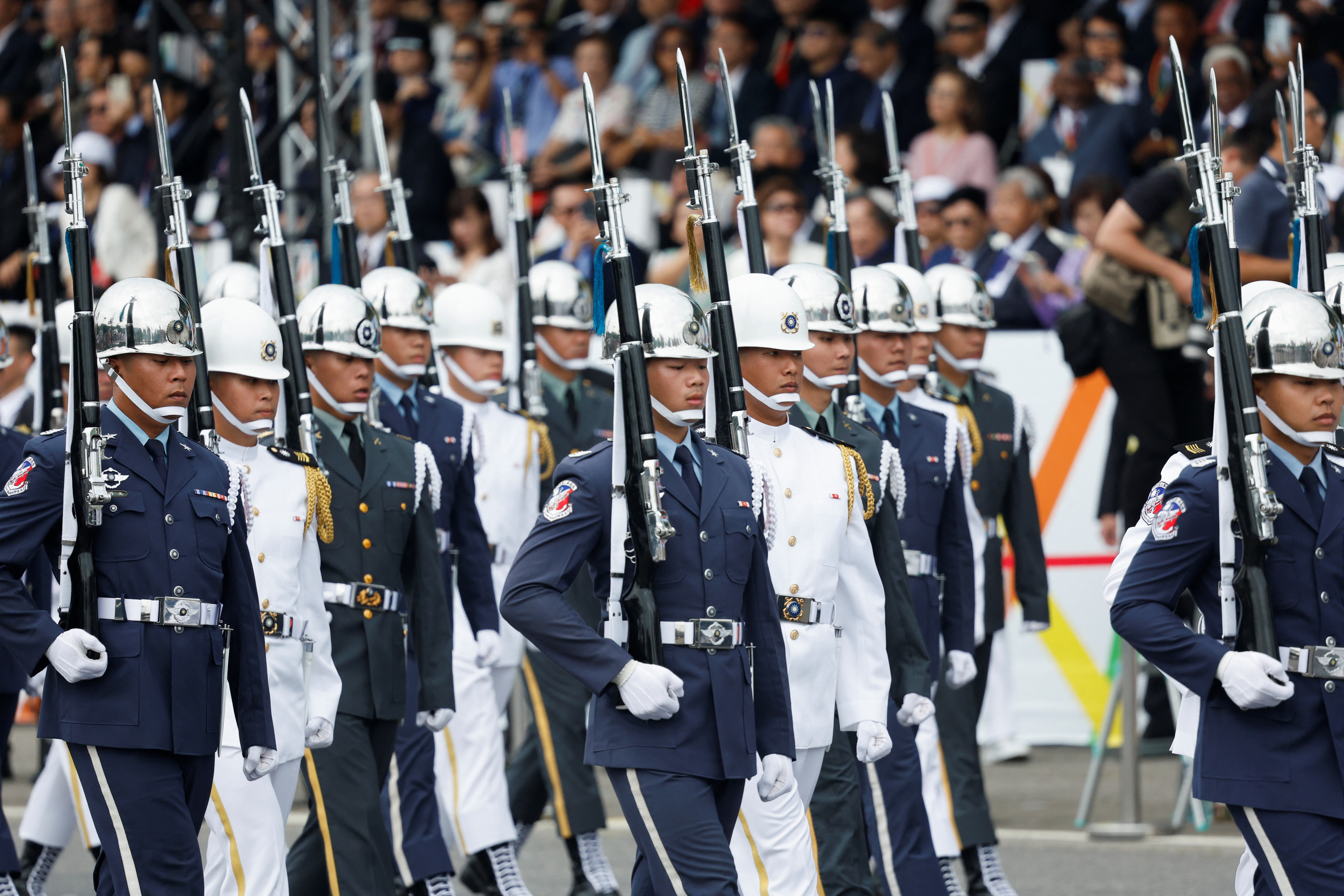 Ceremonial guards marching at the inauguration ceremony. Some are in white uniforms and others in blue. They are carrying rifles with bayonets