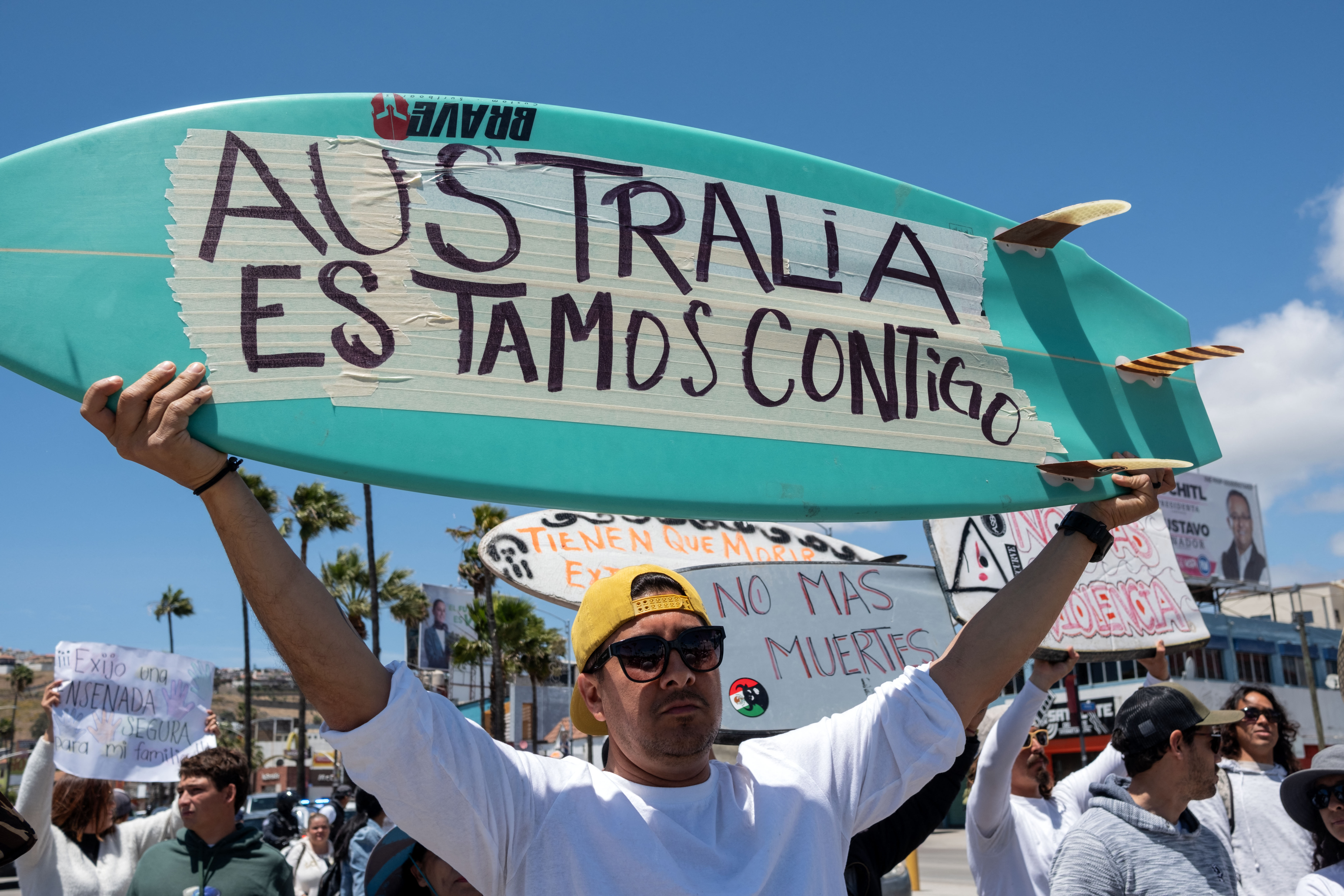 A man raises a surfboard reading 'Australia We Are With You' during a rally in Mexico. Other people are walking alongside him