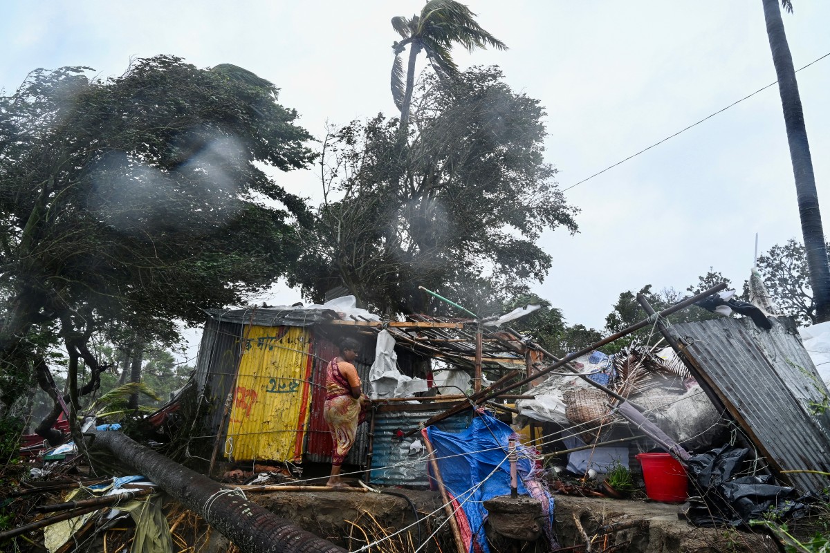 A woman stands next to her damaged house after Cyclone Remal made landfall near a beach in Kuakata