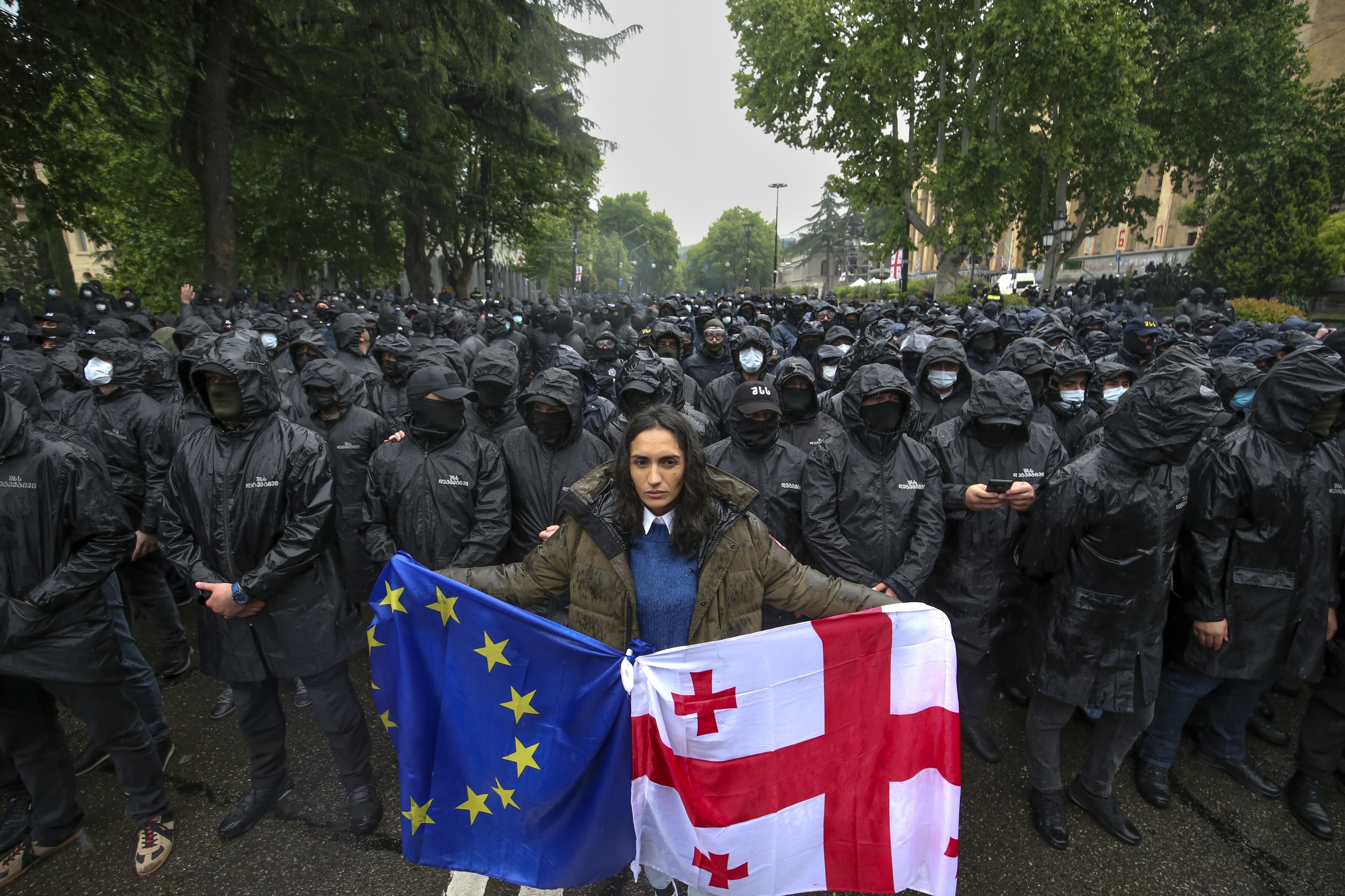 A woman holds a Georgian national and an EU flags in front of riot police blocking a street