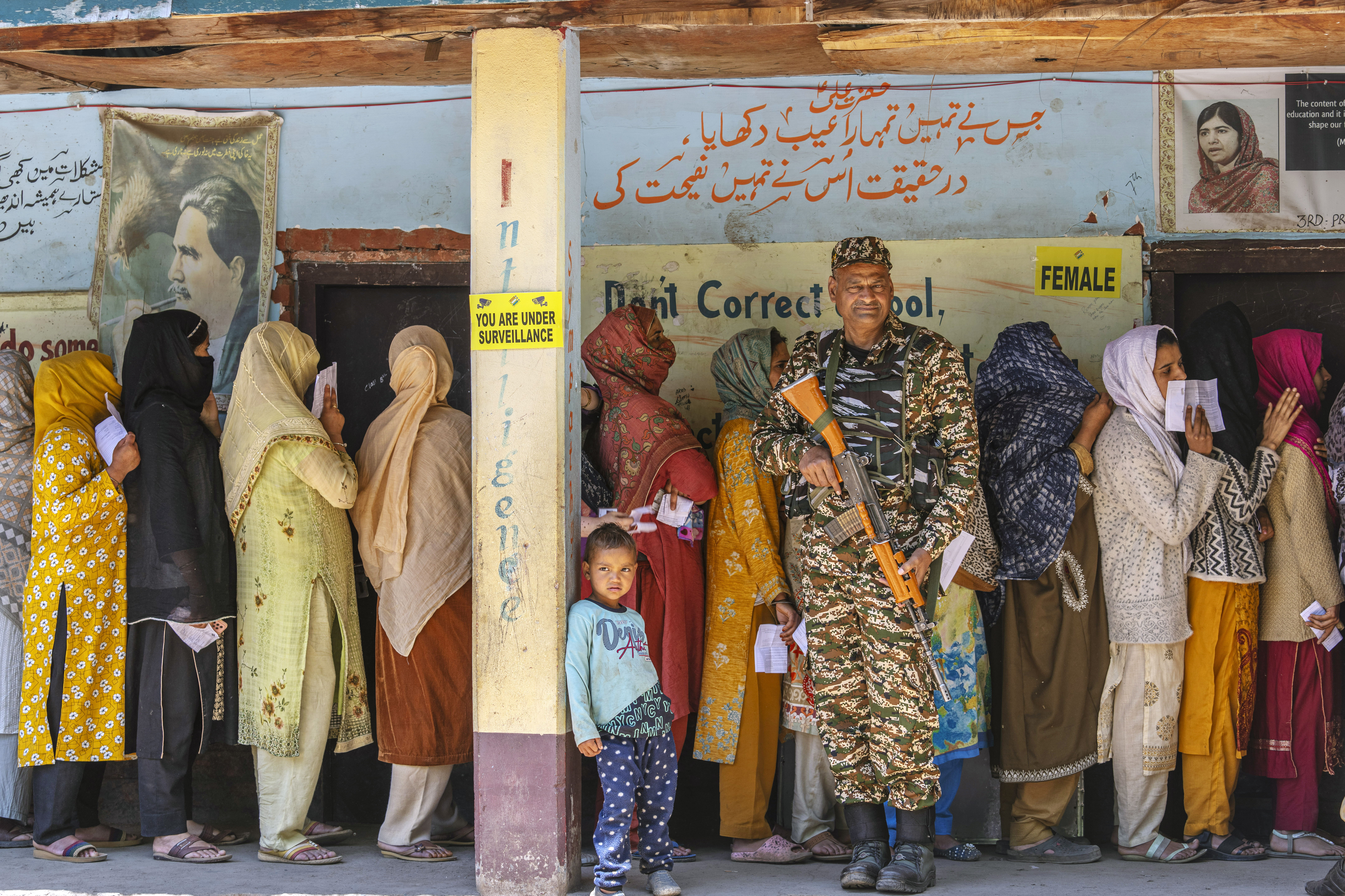 A paramilitary soldier stands guard as Kashmiri women queue up at a polling booth to cast their vote in the sixth round of polling in India's national election in Lidroo, south of Srinagar, Indian controlled Kashmir, Saturday, May 25