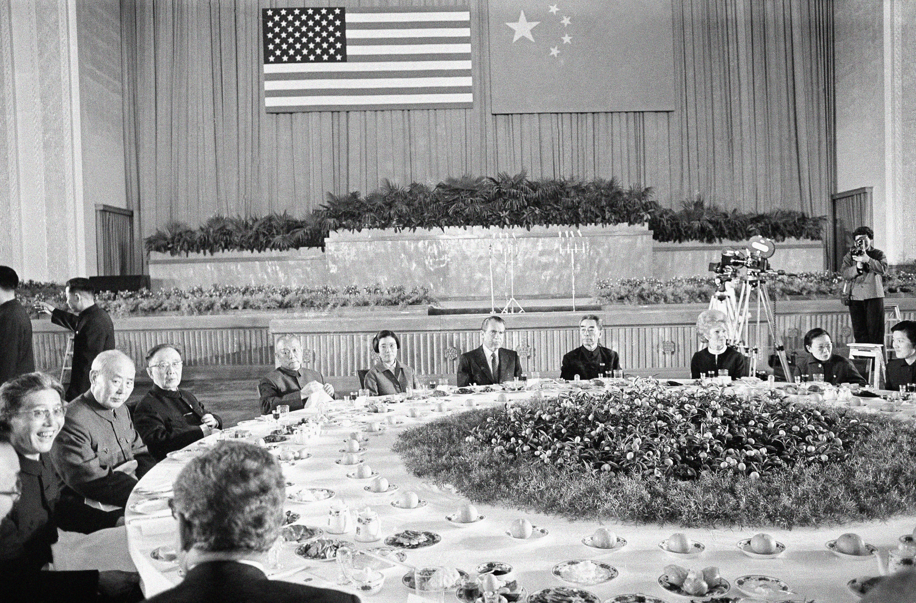 US President President Richard and first lady Pat Nixon at an enormous banqueting table on their visit to China in 1972. Chinese Premier Zhou Enlai is on the far side of the table. The Chinese and US flags are displayed on the wall behind them