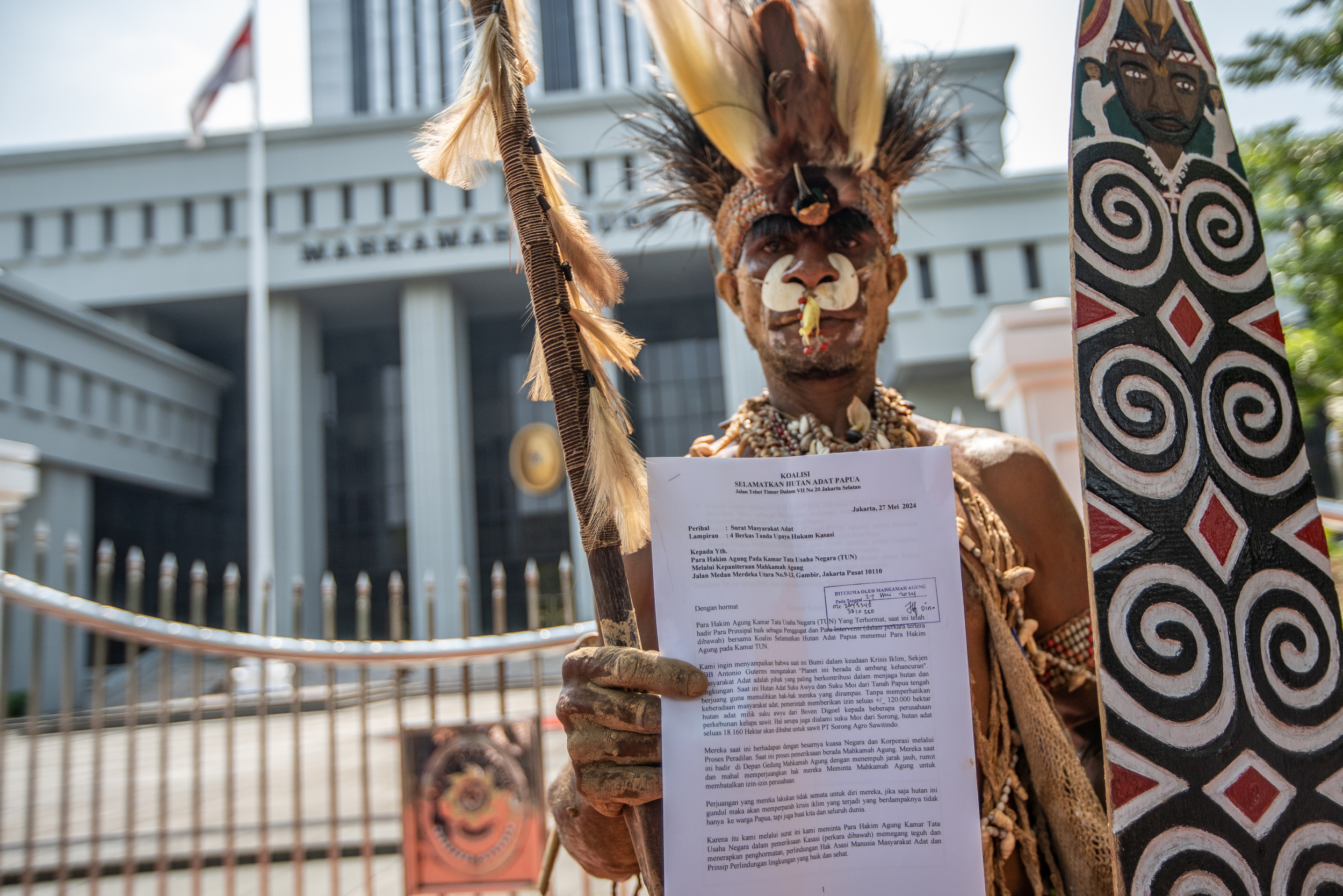 Hendrikus Woro, a representative from the Papuan indigenous community of Awyu, holding a paper showing their concerns. He is in traditional clothing and is also carrying a staff and shield.