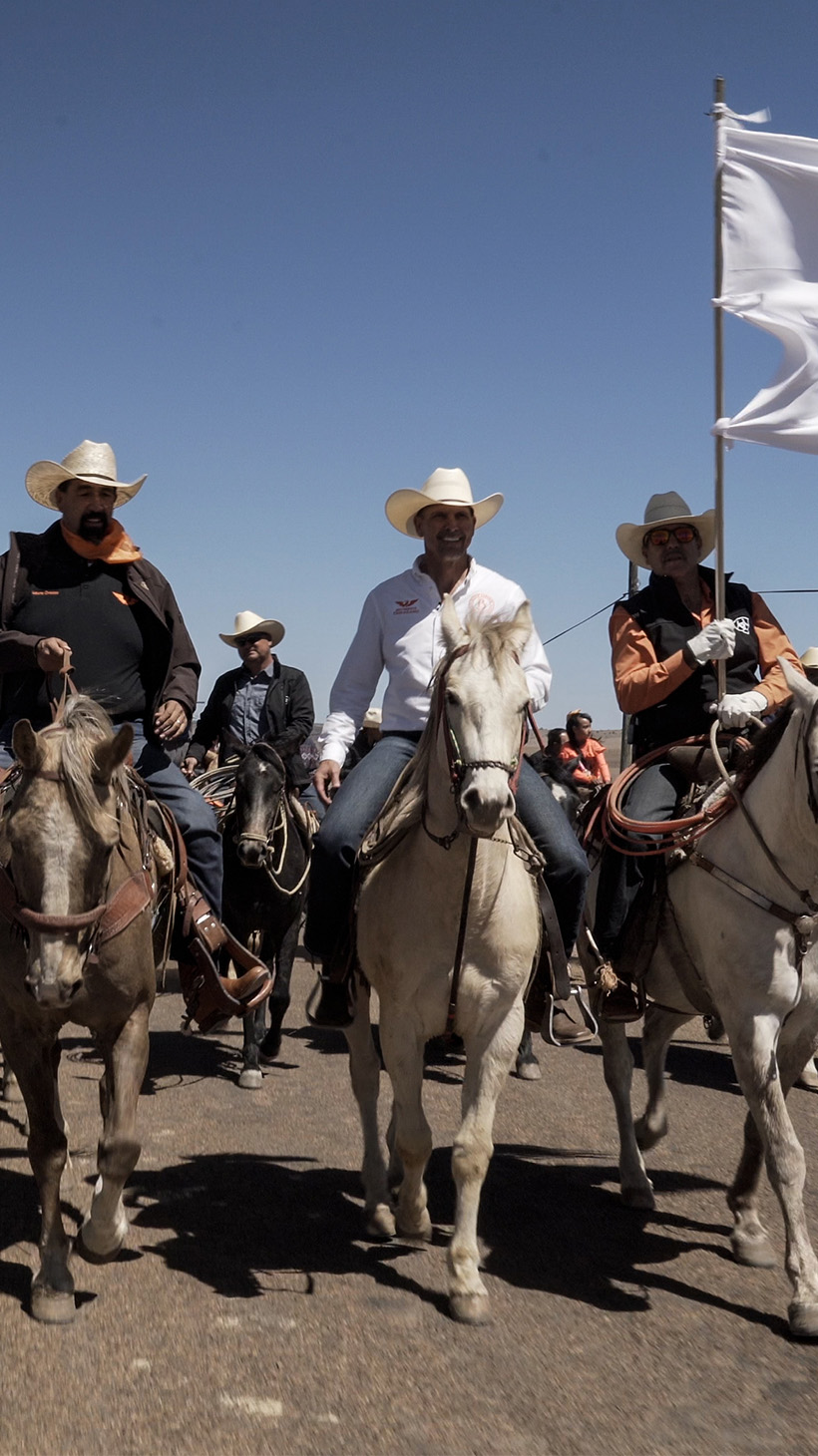 A line of political candidates and their supporters ride horses in the north Mexican desert.