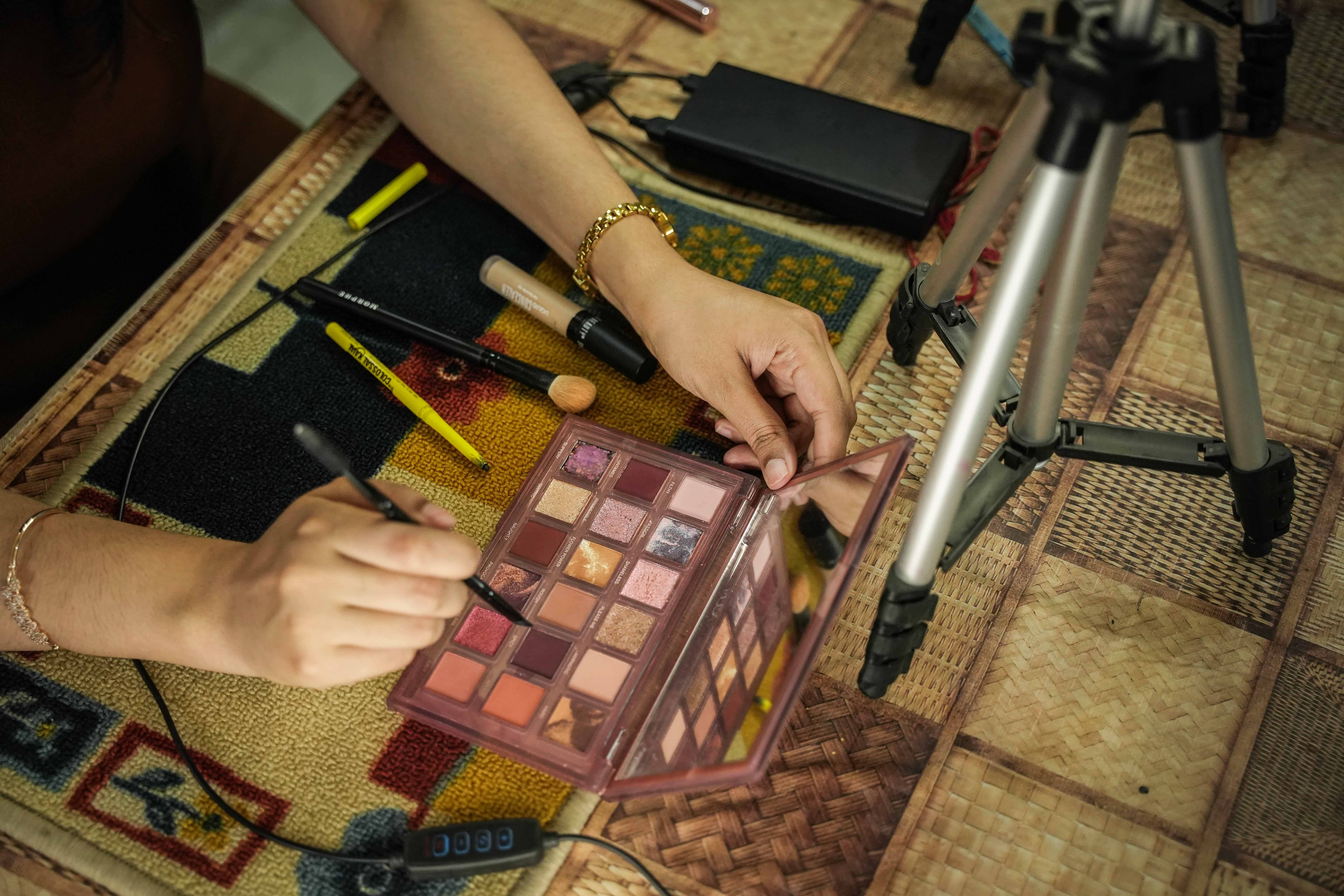 A spread of makeup palettes, brushes, and mascara in front of Sharma which she uses during her recording for makeup. (Md Meharban/Al Jazeera)