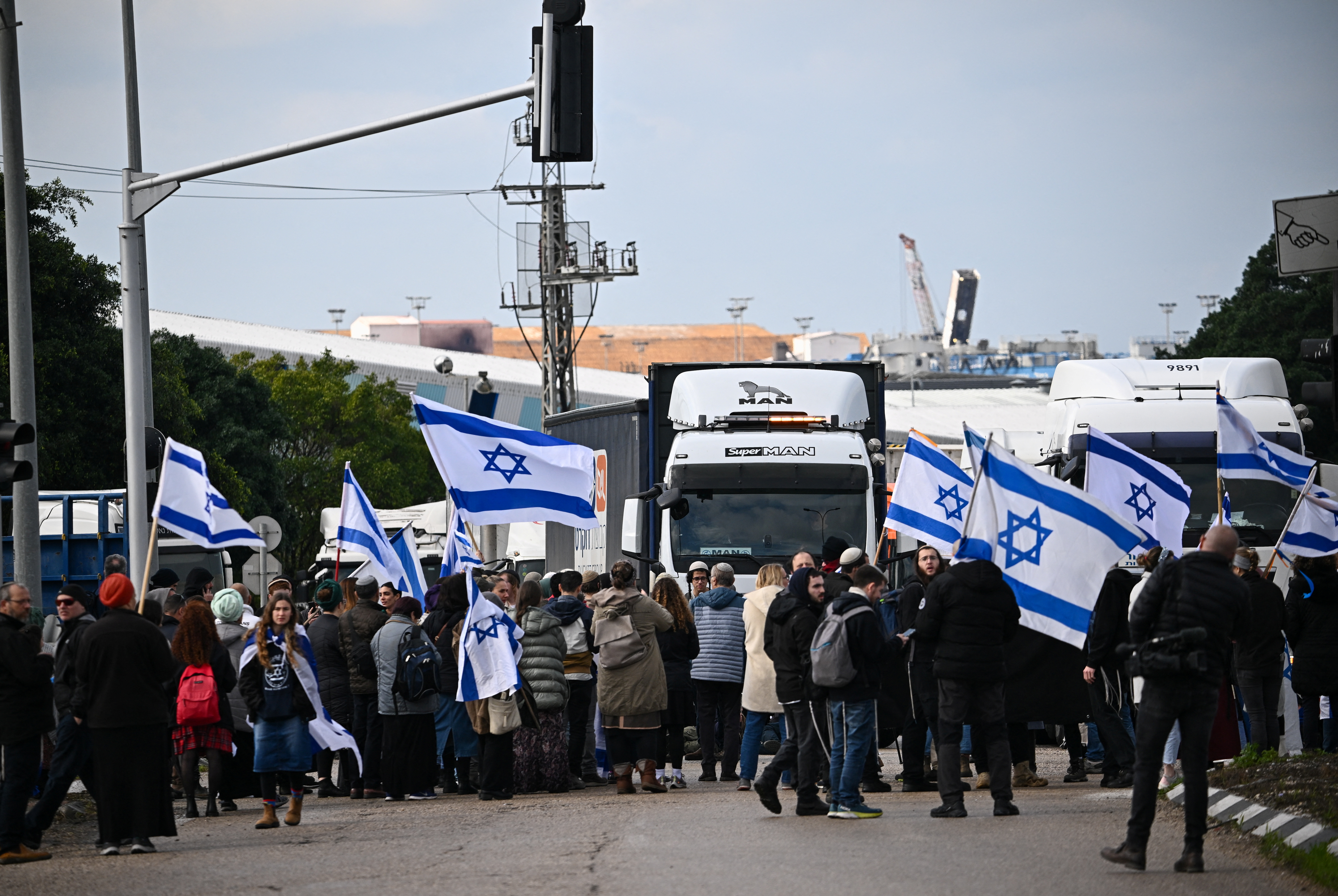 Dozens of people wave Israeli flags in front of trucks on a road