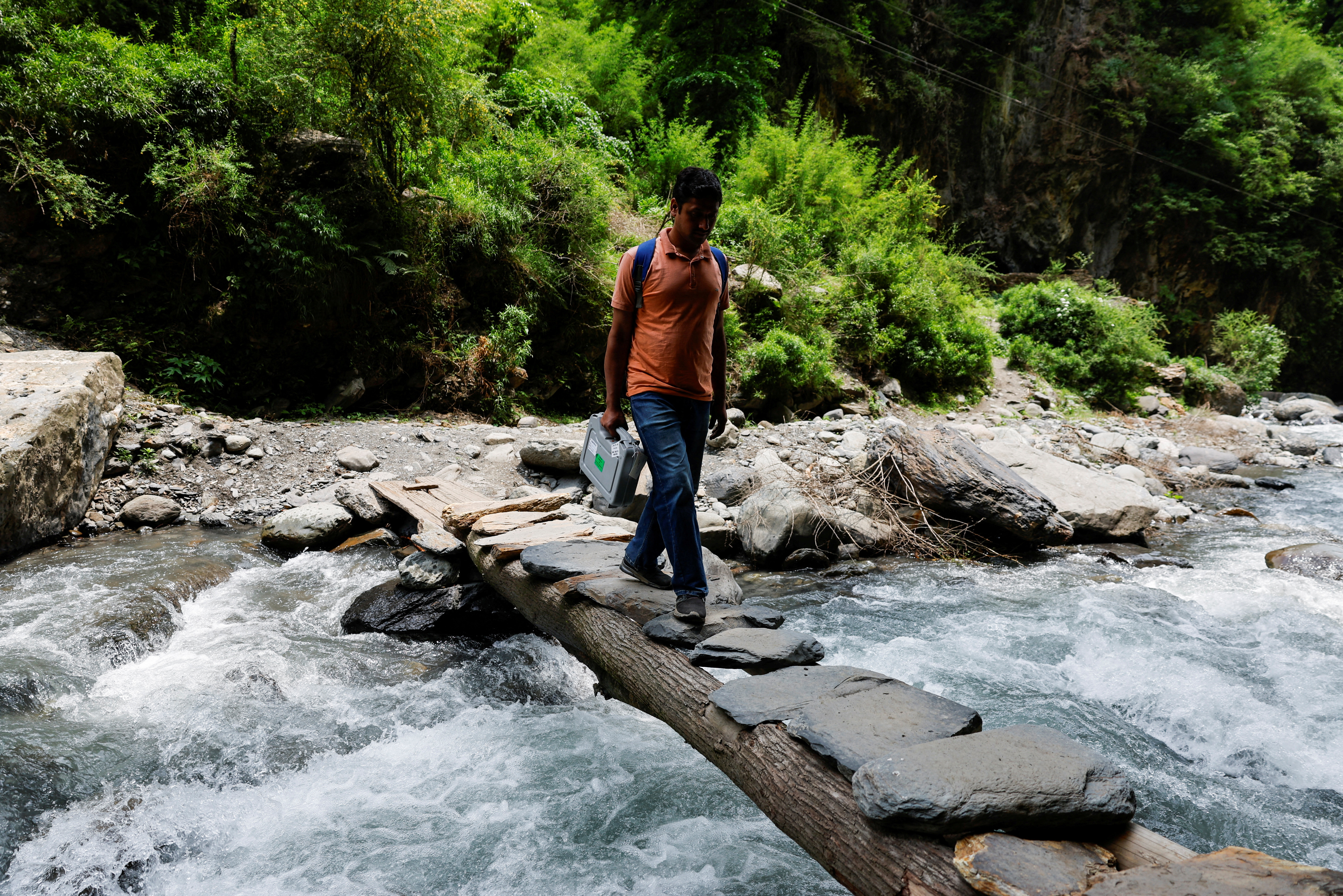 Krishanchand Sharma, a Polling Officer, crosses a river on a makeshift bridge made of stones and tree logs during a trek in the mountains to reach a remote polling station, ahead of the seventh and final phase of the elections, in Almi, Chamba, in the northern state of Himachal Pradesh, India, May 30