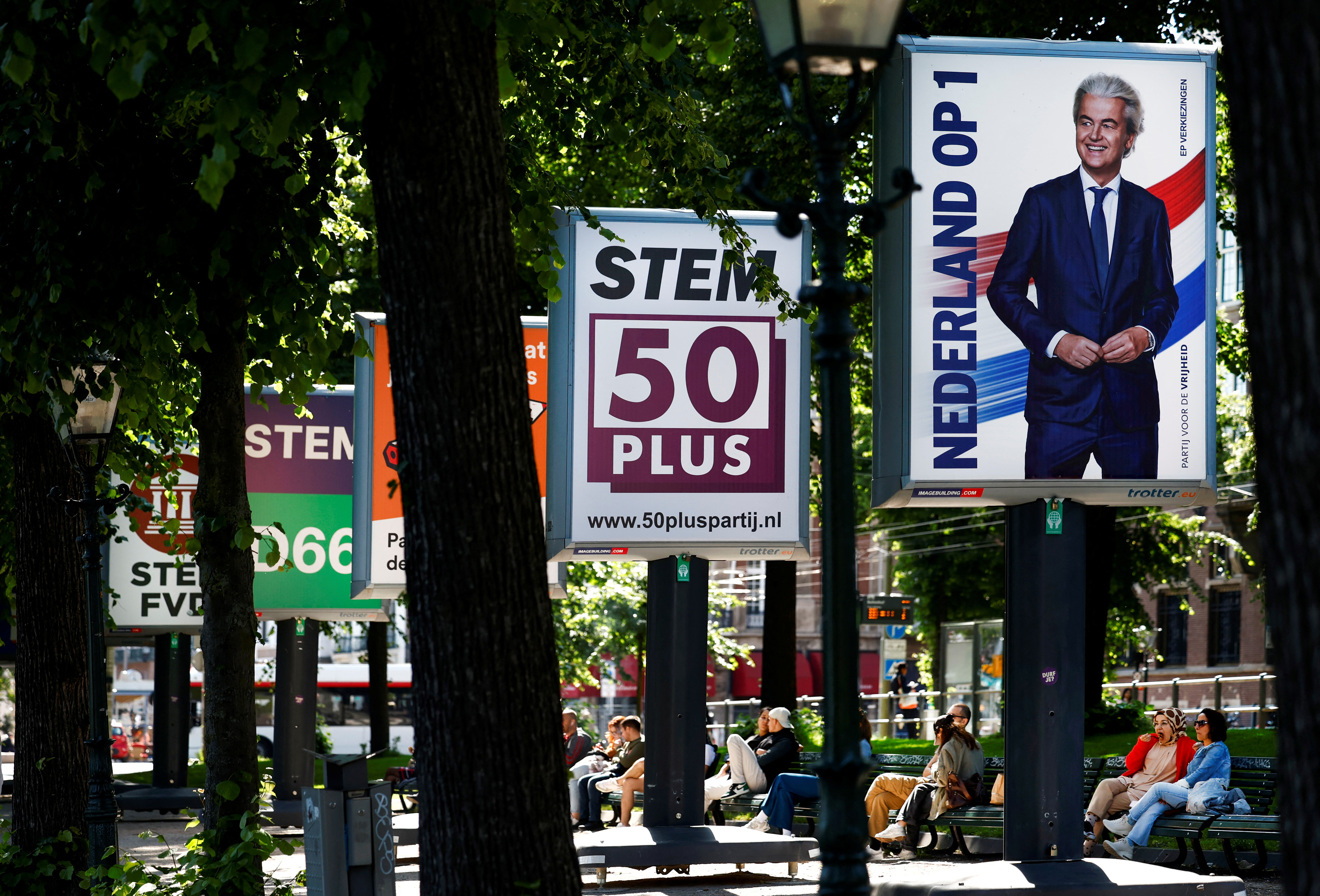 People sit near the election campaign boards, ahead of the elections across 27 European Union member states, of which the Netherlands is the first country to go to the polls in this round of elections