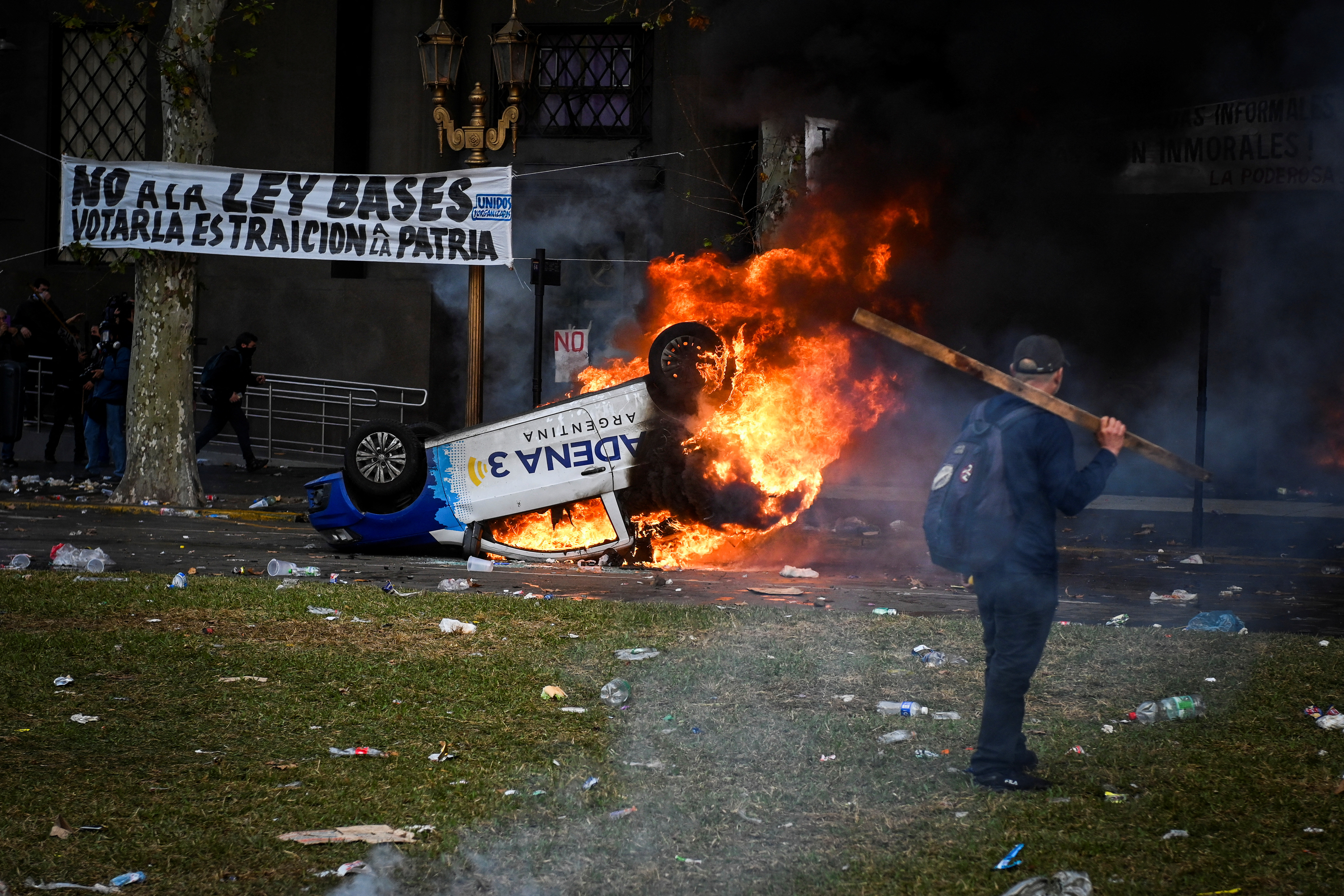 A car burns outside in Buenos Aires, as a protester with a wooden plank stands nearby