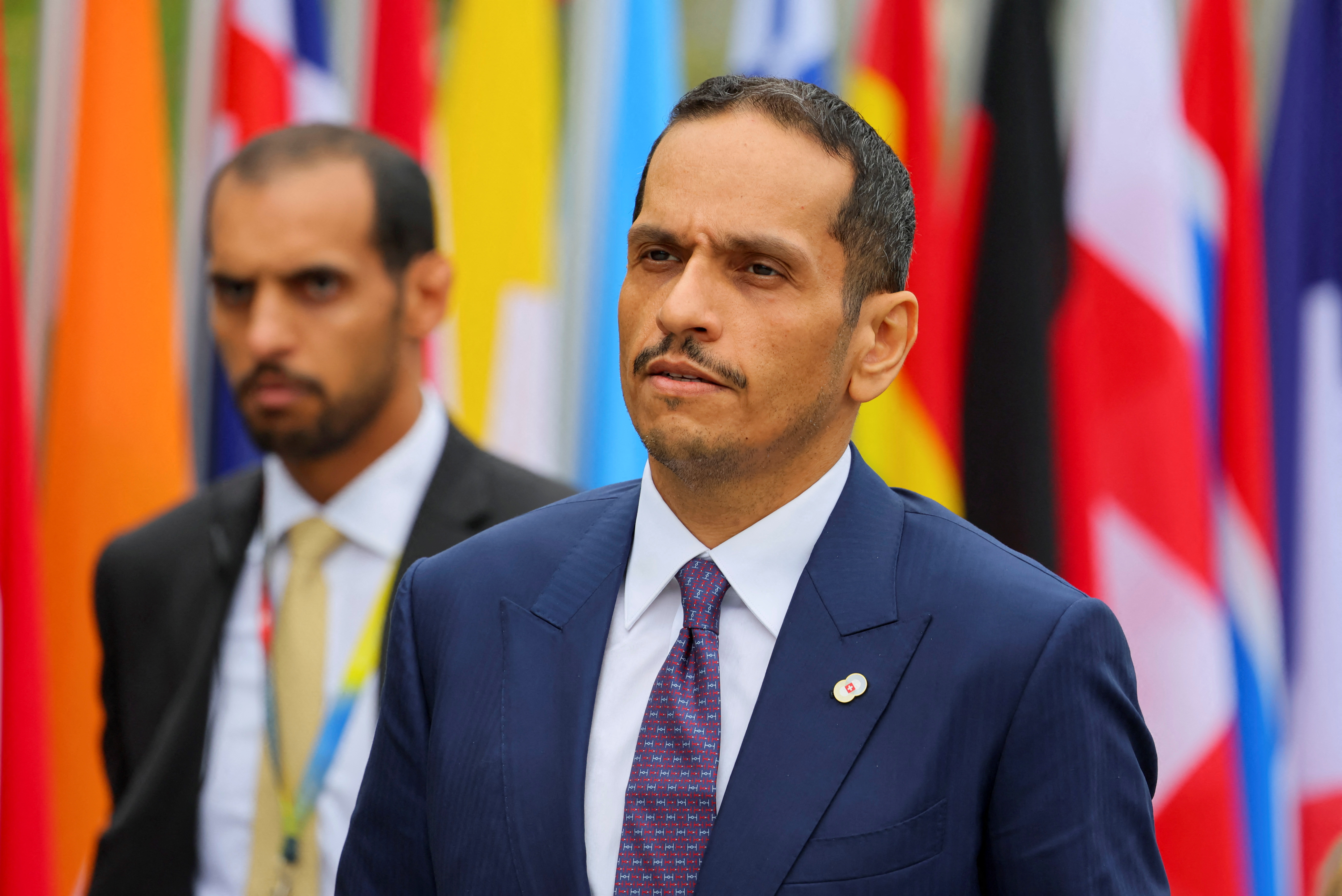 a man in a suit with a moustache stands in front of flags