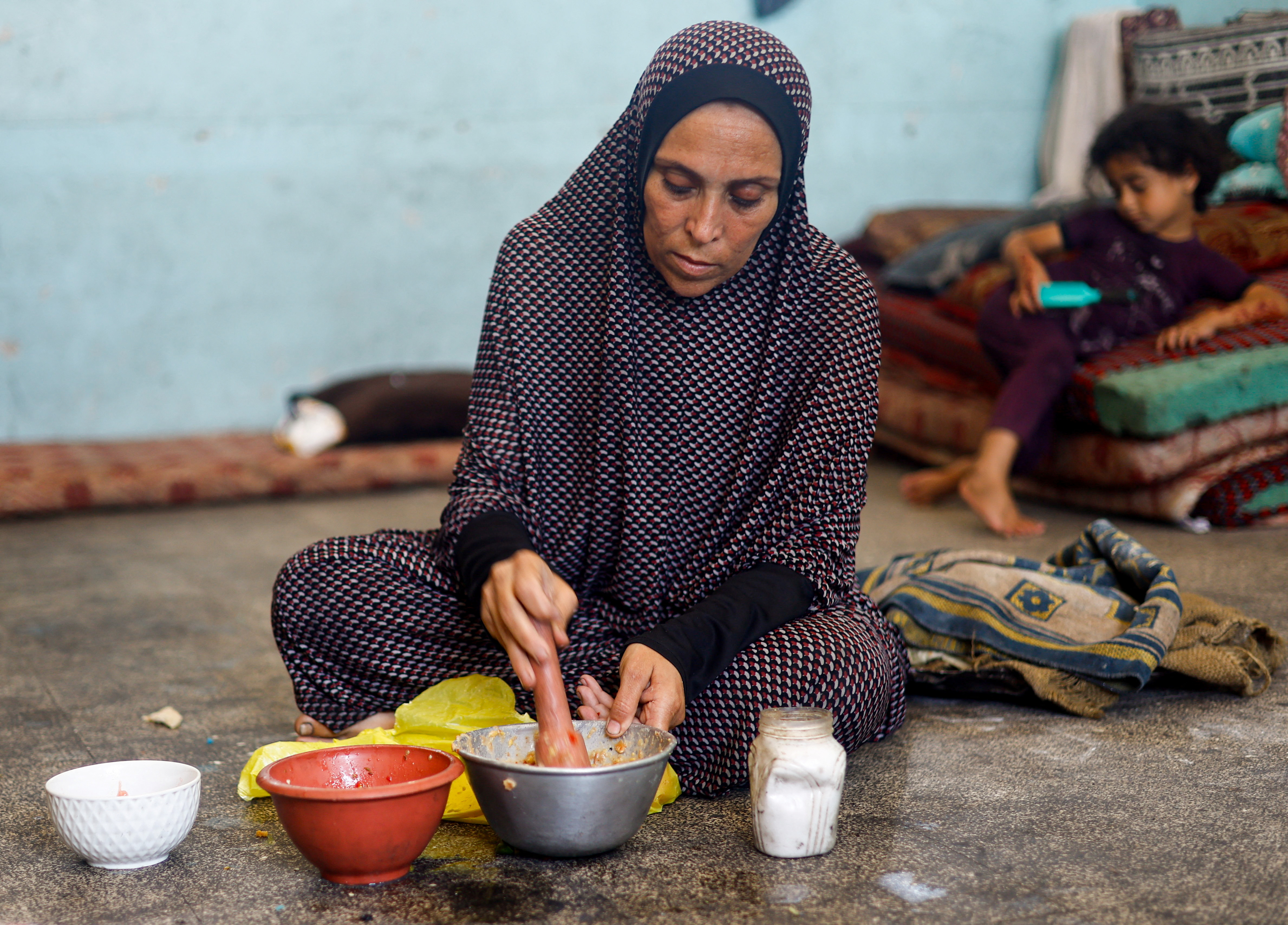 A displaced Palestinian woman prepares food at a school classroom where she shelters, amid food scarcity