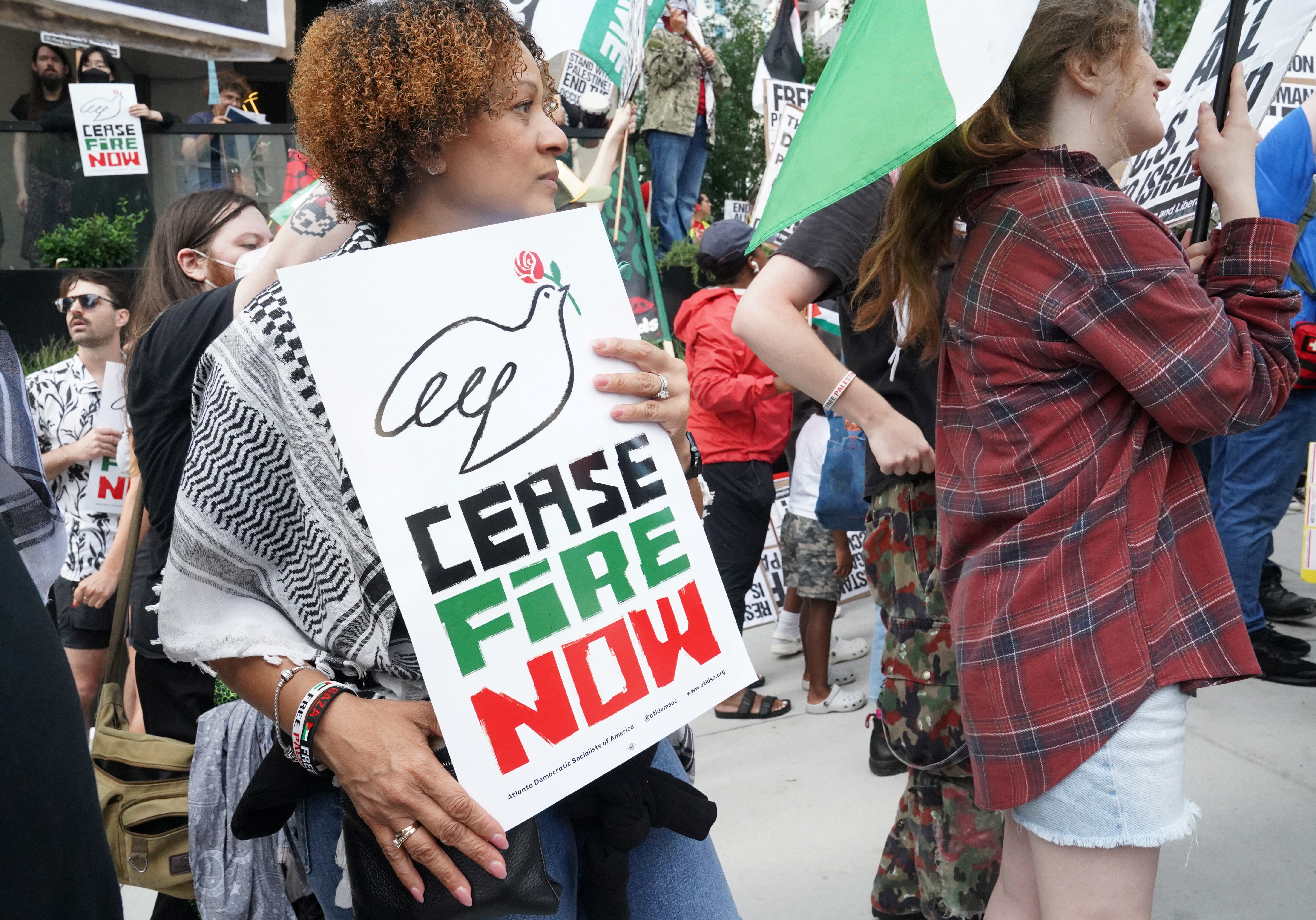 Protesters hold up signs that say, "Ceasefire now."