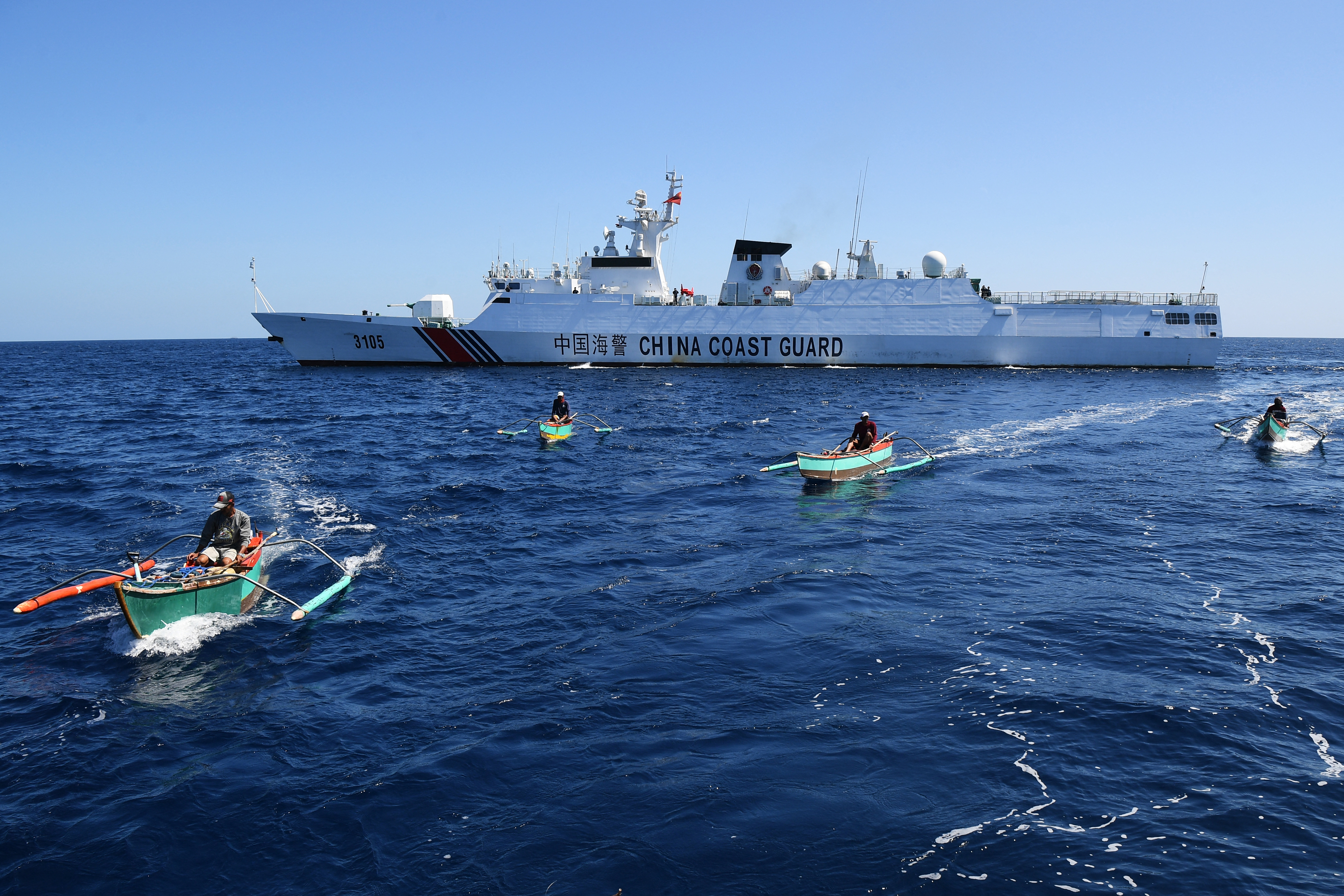 Filipino fishermen aboard their wooden boats sailing past a Chinese coast guard ship near the disputed Scarborough Shoal.