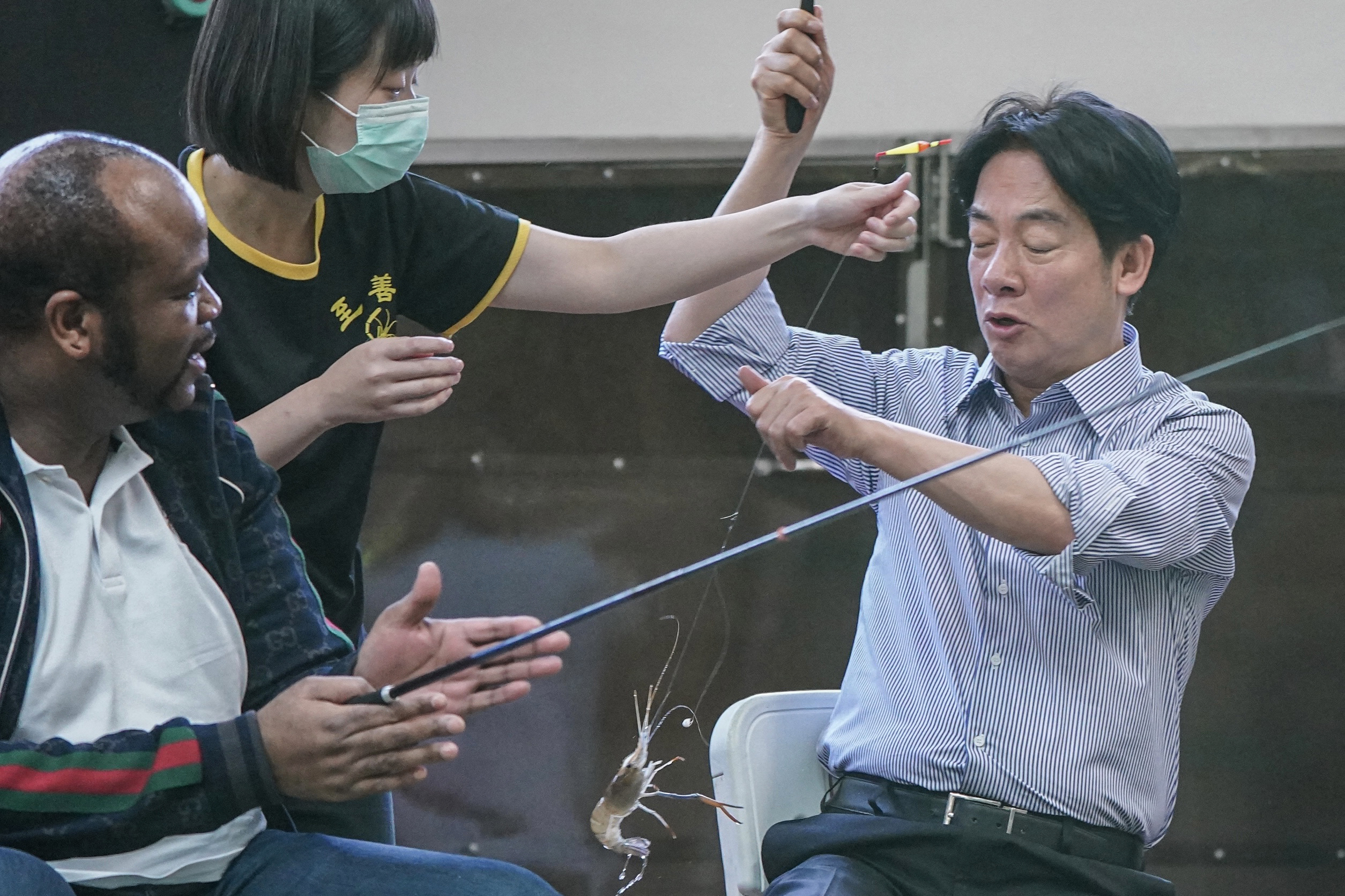 William Lai and King Mswati III of Eswatini fishing for prawns at a shrimp farm in Taiwan. Lai has just caught a prawn and it's dangling from the rod. The king is clapping. They look happy and relaxed.