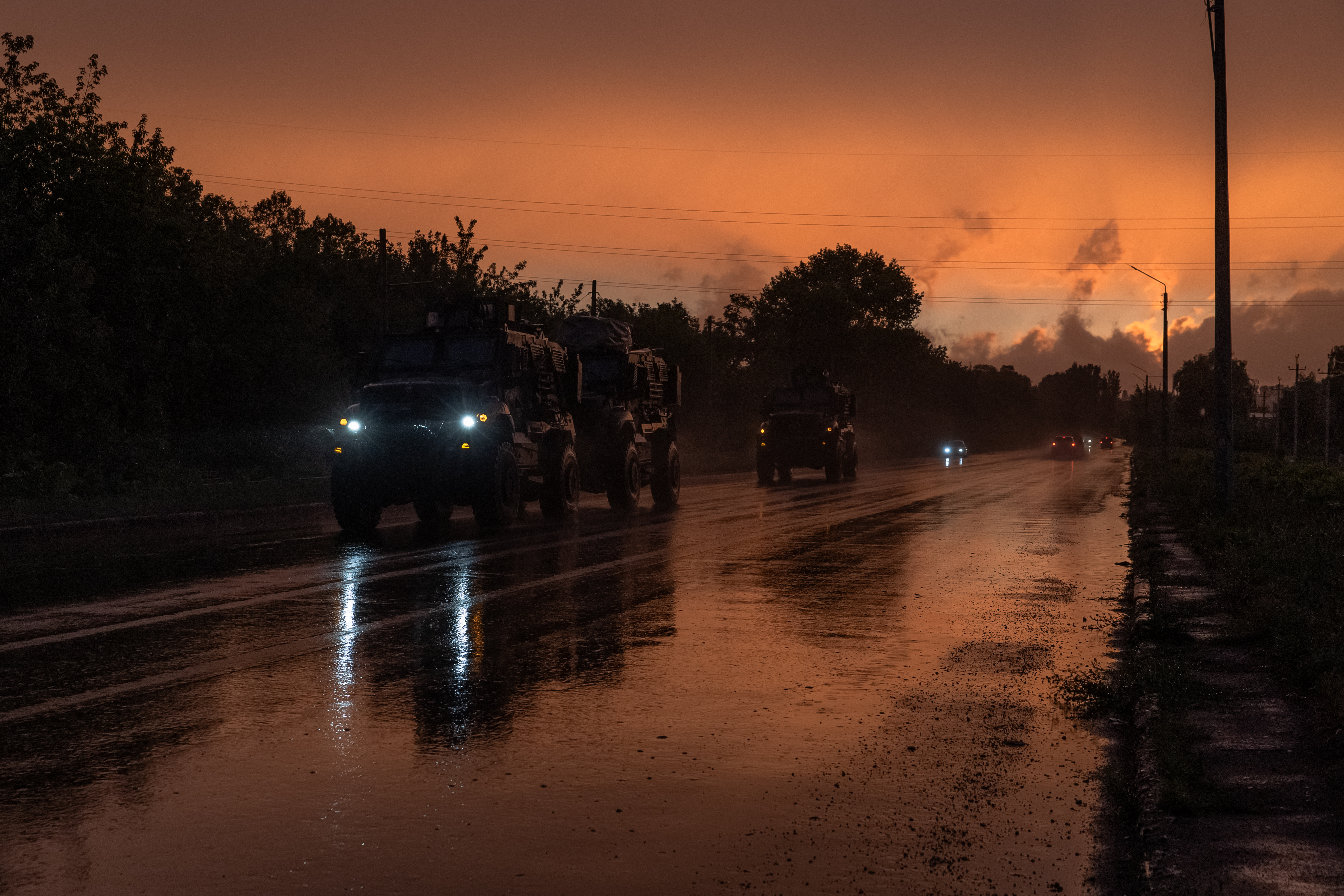 Ukraine military vehicles on a dark road in the eastern Donetsk region. The sky behind them is orange.