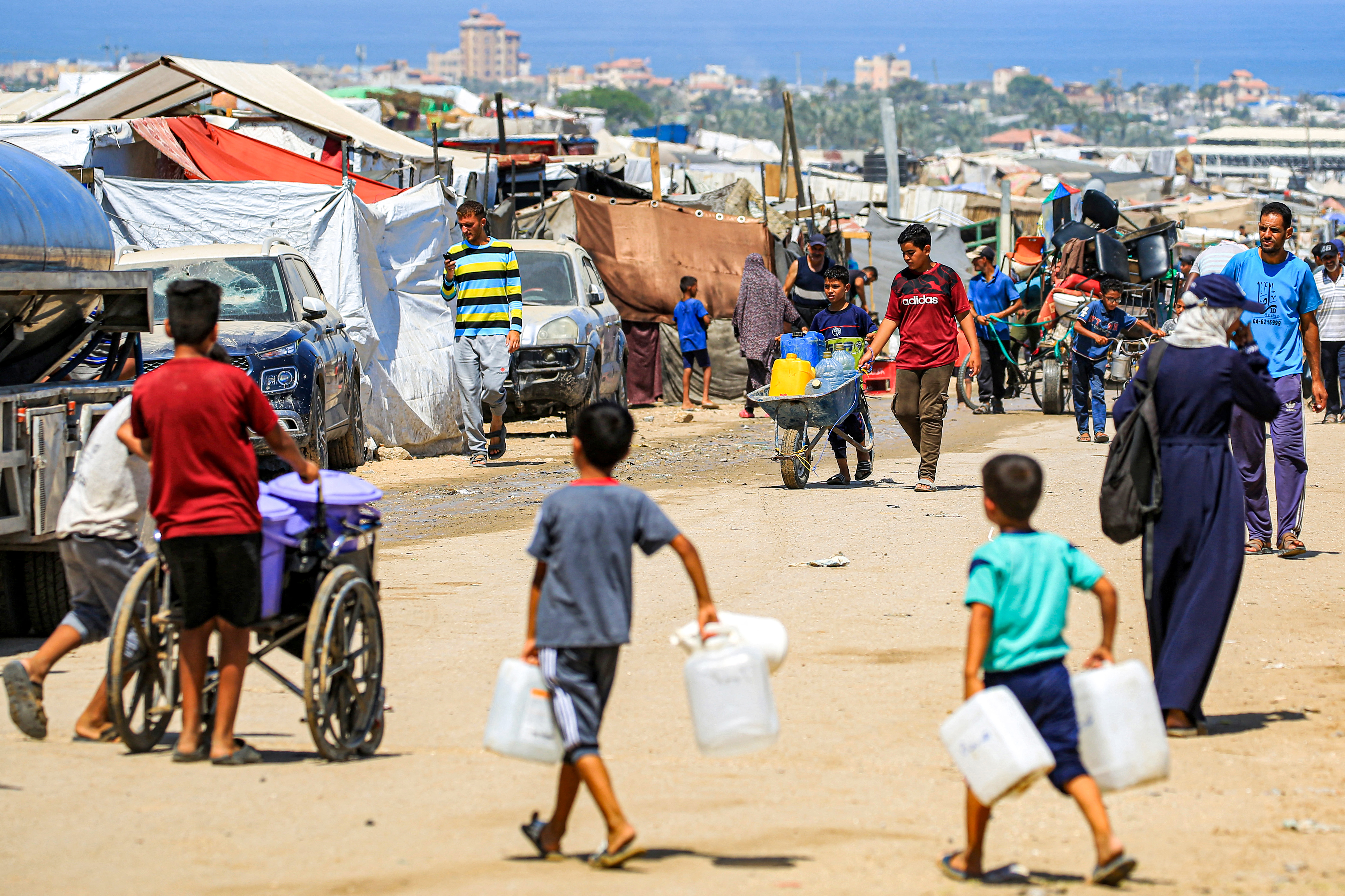 Boys walk with jerrycans to fill up from a water truck in Rafah in the southern Gaza Strip